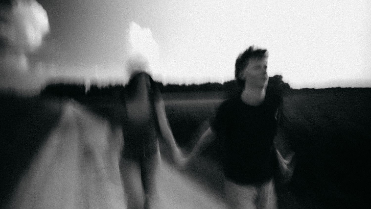 Blurry black and white photo of two people holding hands running down a rural road.