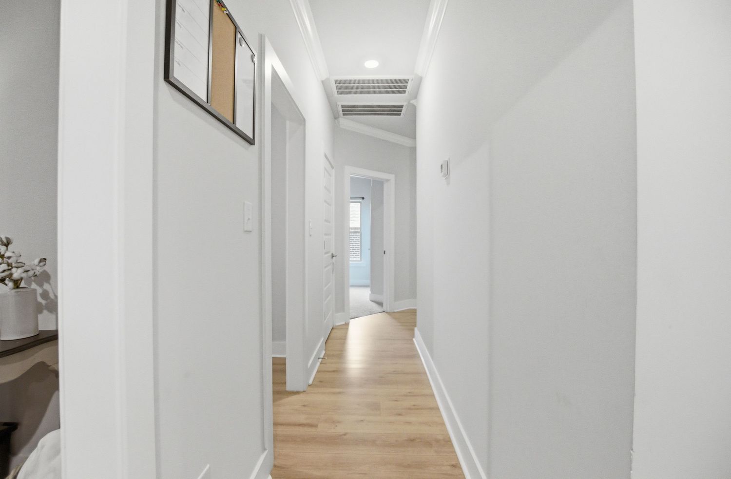 Bright white hallway with light hardwood floors, recessed lighting, and multiple doorways.