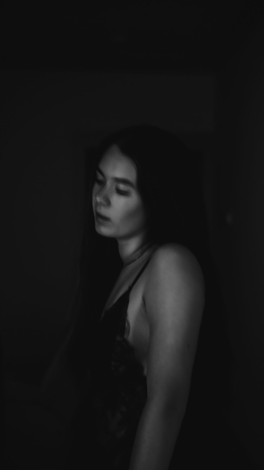 Black and white portrait of a young woman with long dark hair posing in dramatic low-key lighting.
