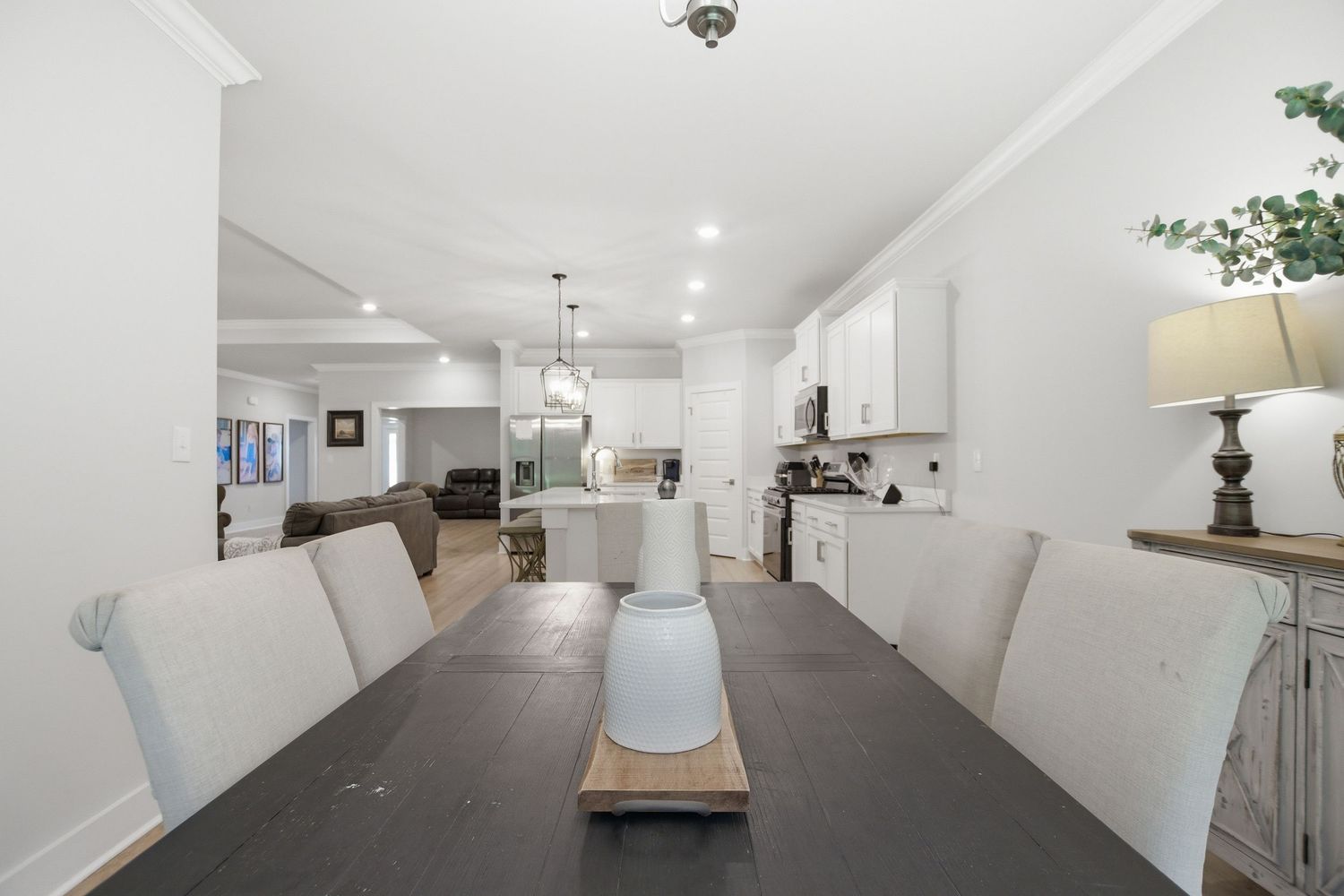 Open concept dining and kitchen area with white cabinets, dark wood table, and recessed lighting.