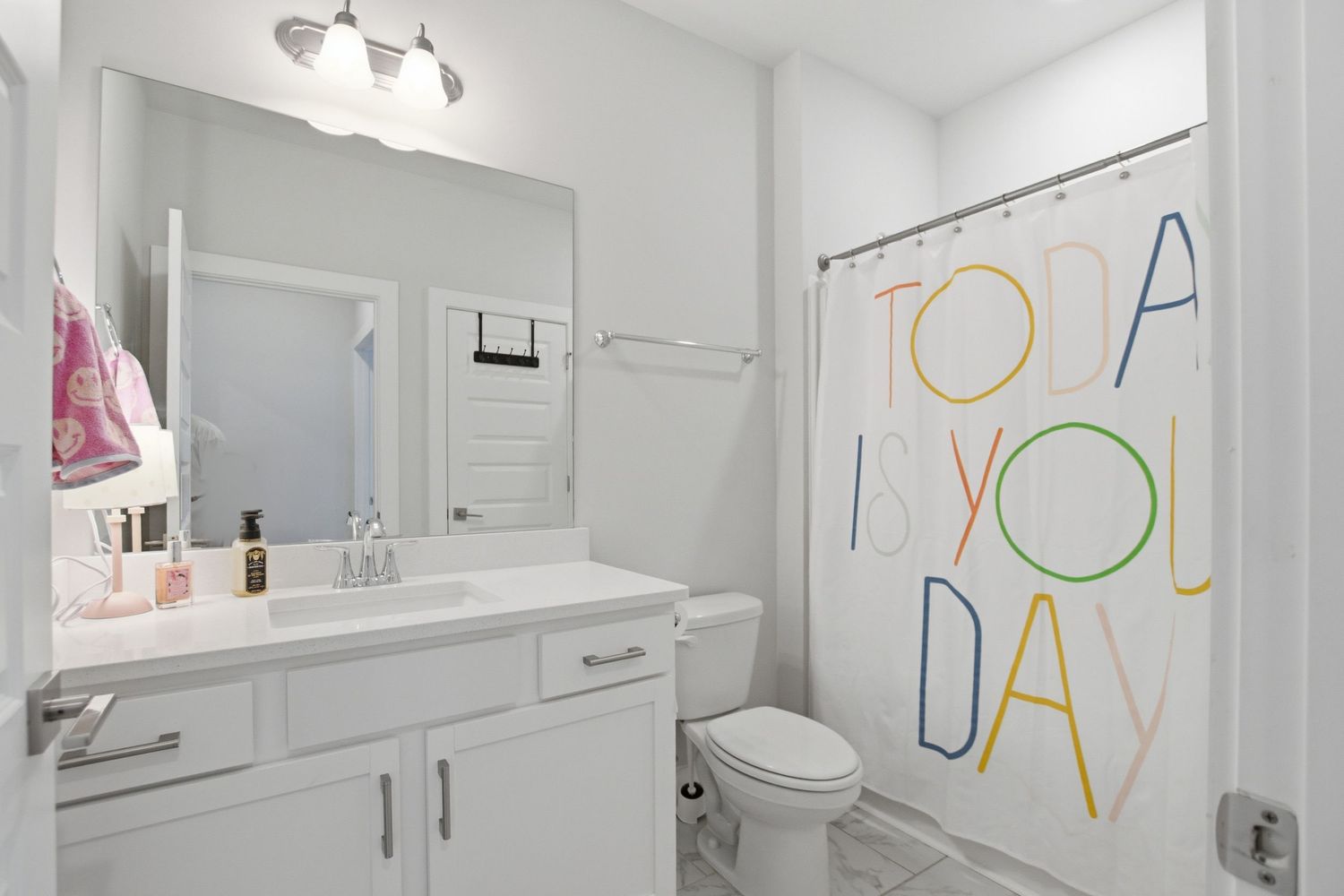 Modern white bathroom with vanity, mirror, toilet, and colorful 'Today Is Your Day' shower curtain.