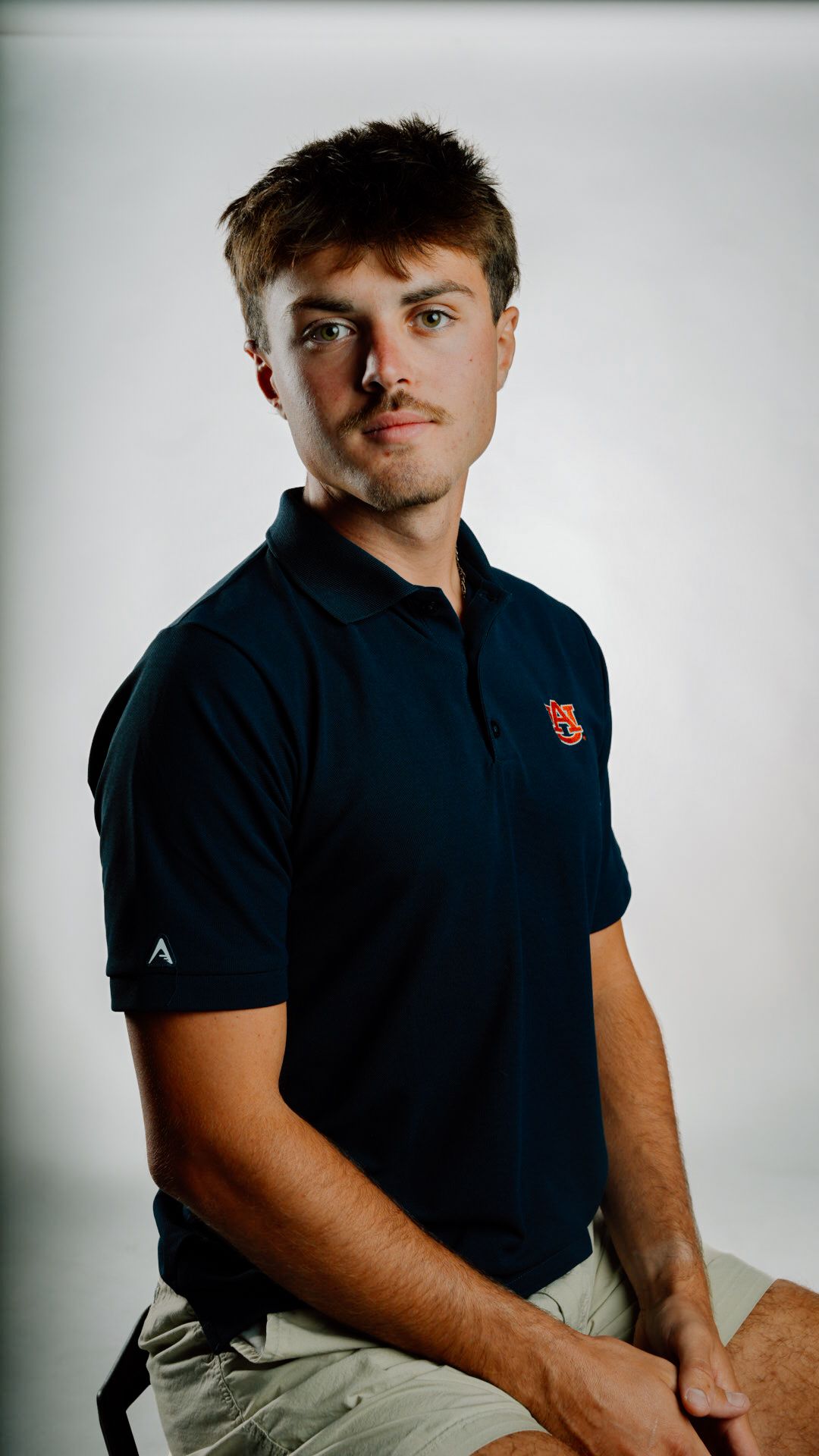 Young man in navy Auburn University polo shirt sitting against white background for a professional portrait.
