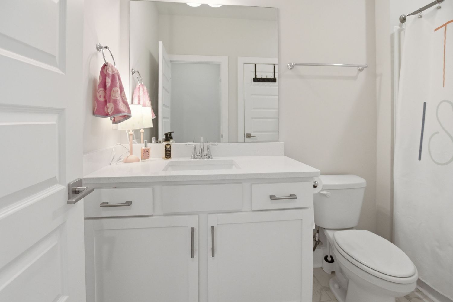 White bathroom vanity with large mirror, white cabinetry, and toilet in a bright clean bathroom.