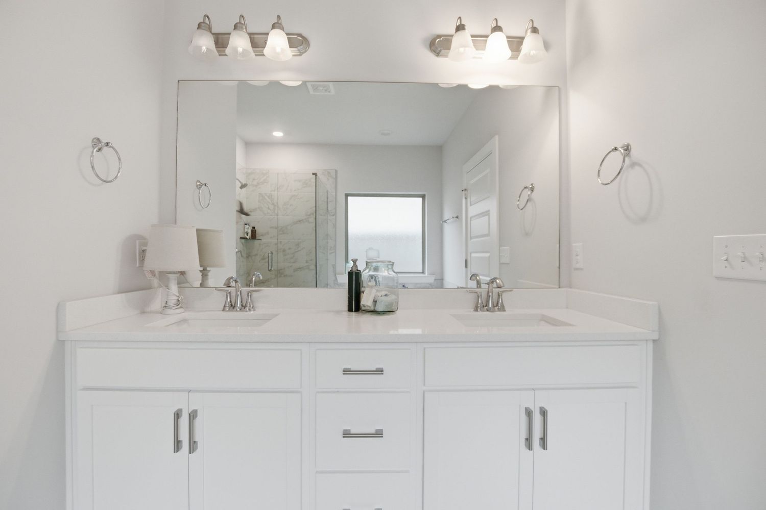 Modern white double vanity bathroom with large mirror, dual sinks, and elegant light fixtures.
