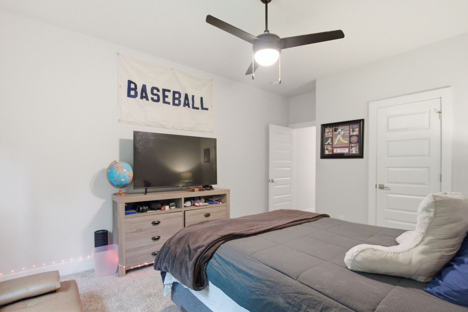 Kids bedroom with baseball theme, ceiling fan, TV on dresser, and comfortable bed.