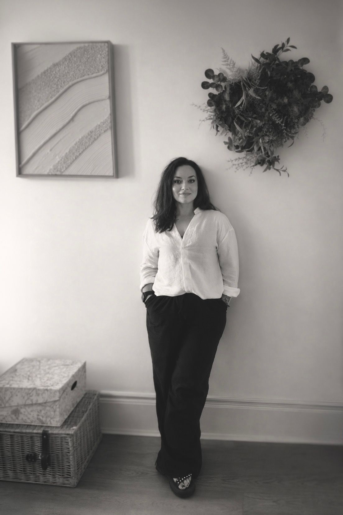 Black-and-white portrait of psychotherapist standing in a minimalist therapy space, wearing a white blouse and black trousers