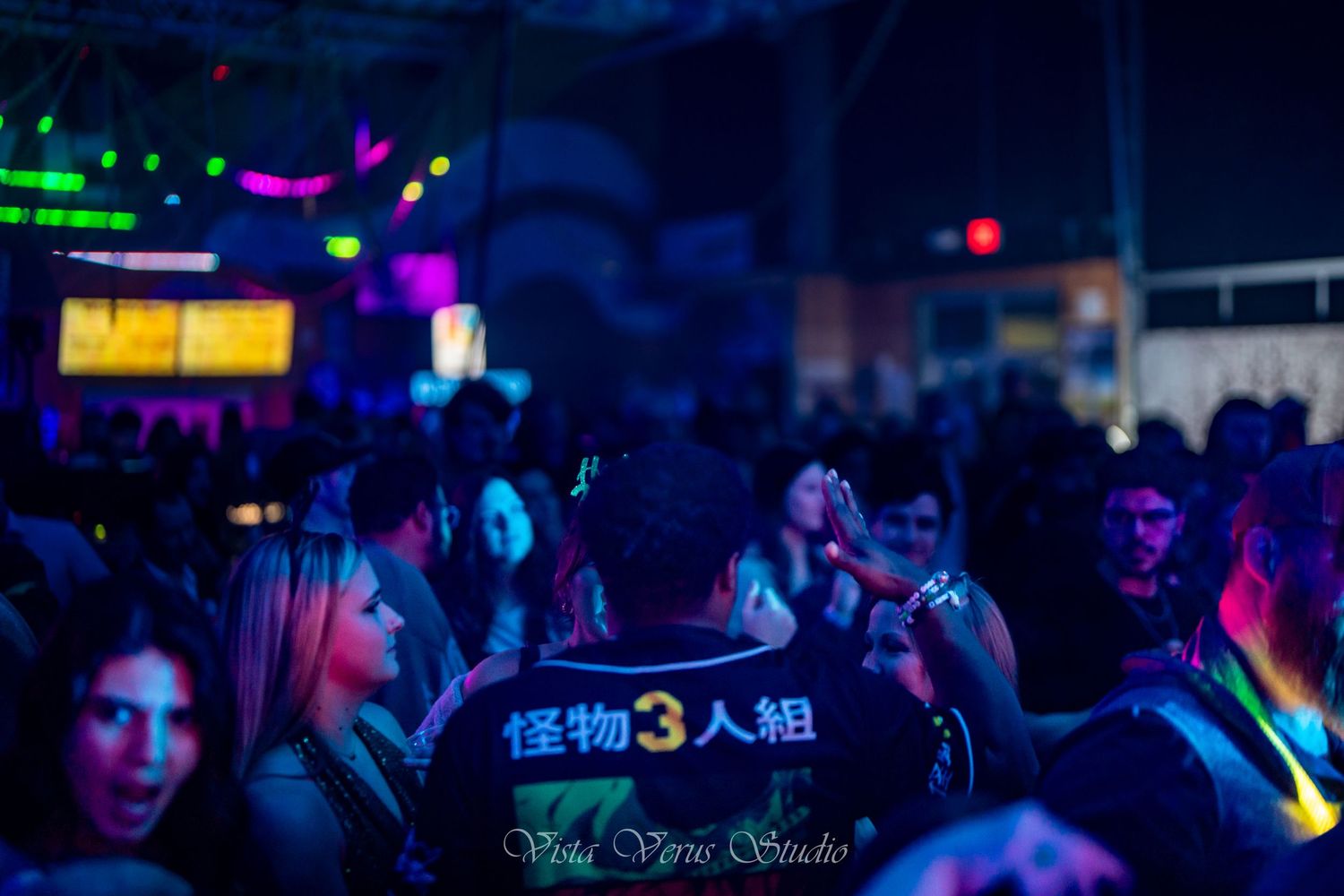 Crowded nightclub scene with colorful lighting and silhouetted audience members.