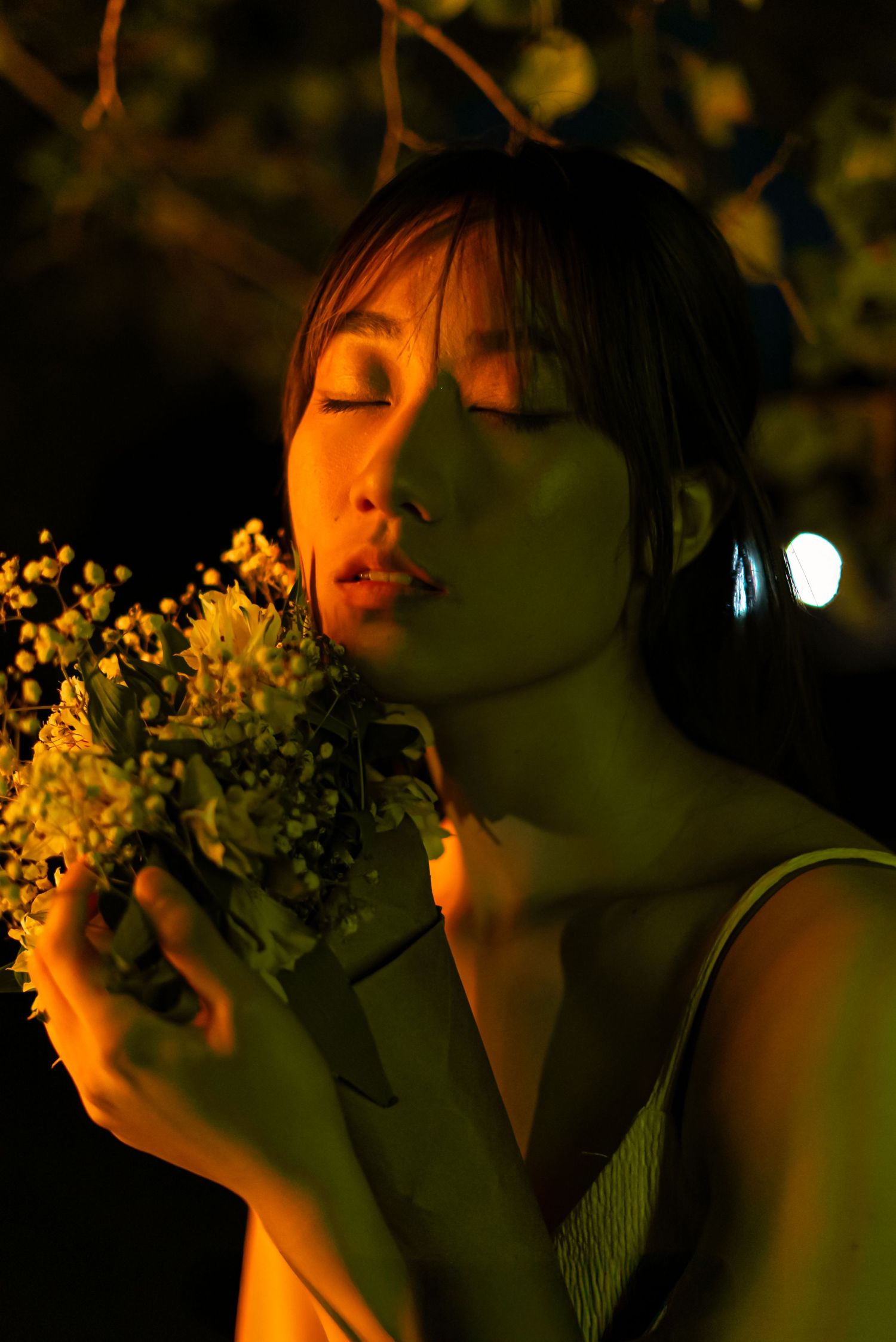 Atmospheric nighttime portrait of someone holding delicate flowers in warm golden lighting.