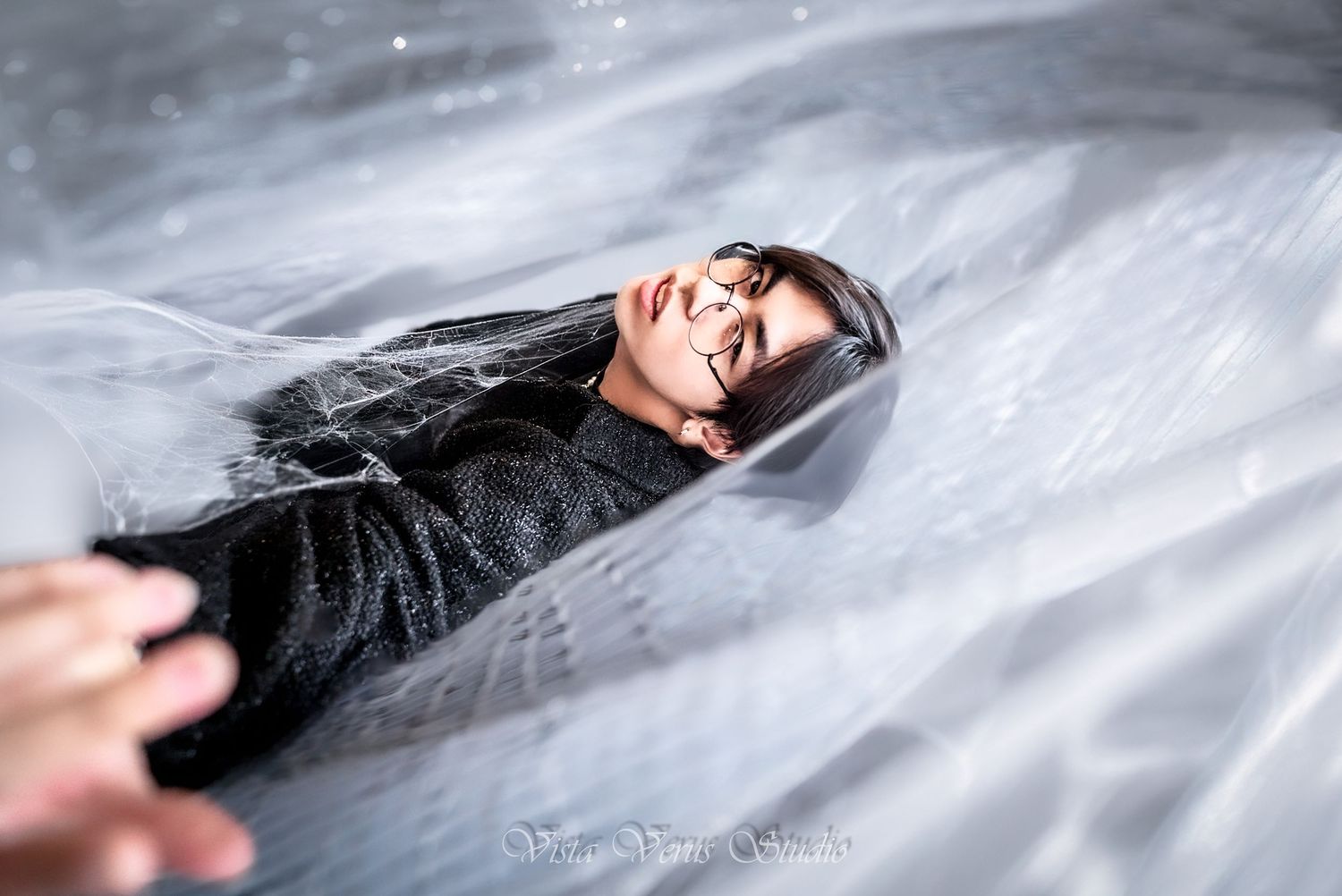 Artistic portrait of person lying under sheer white fabric with moody lighting.