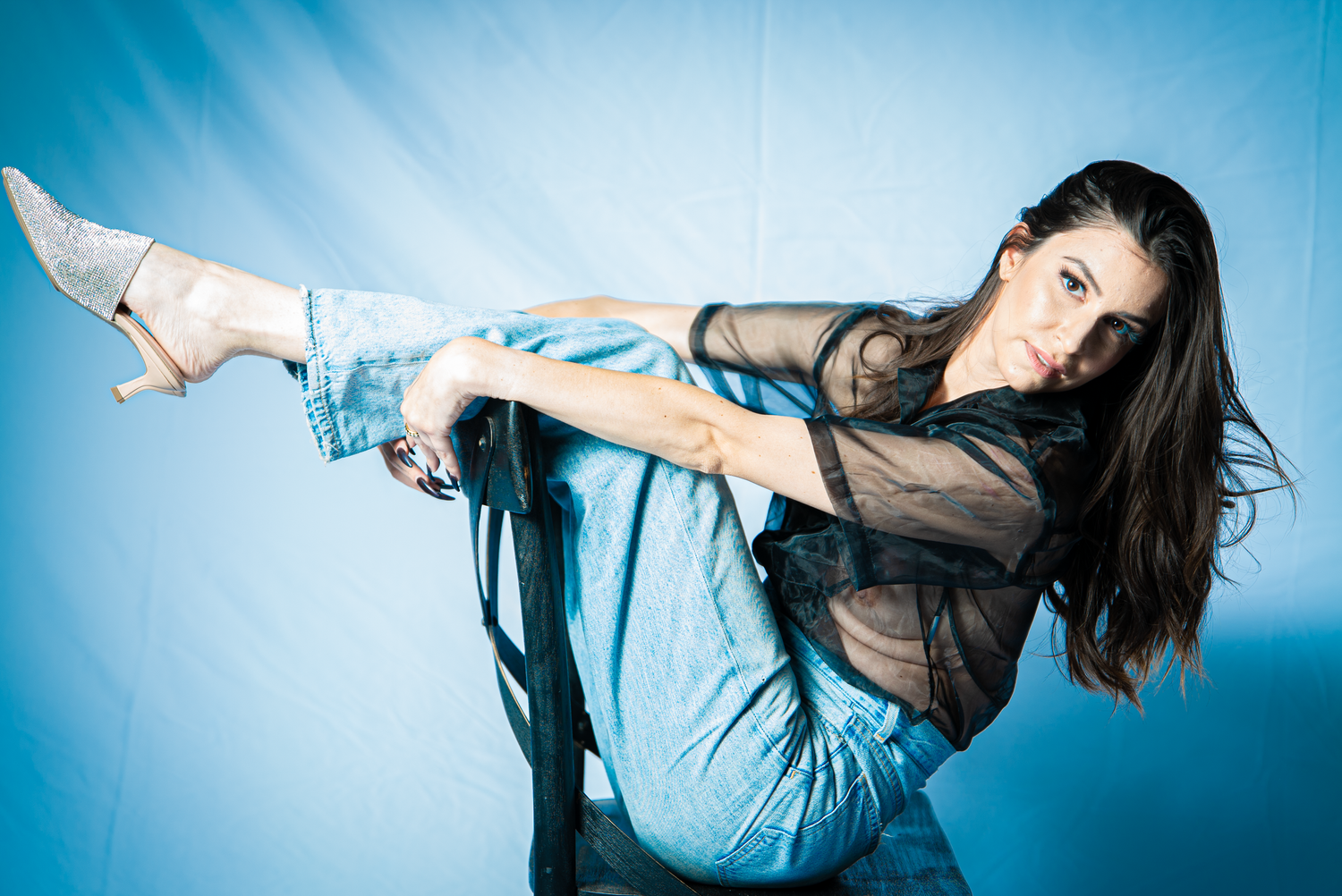 Dynamic dance pose against blue background in sheer top and jeans.