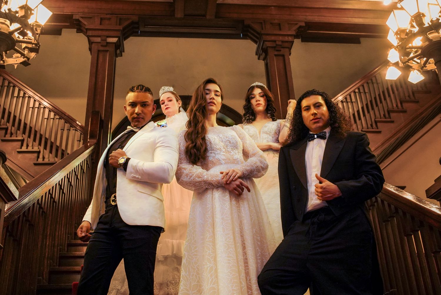 Wedding party poses dramatically on grand wooden staircase in formal attire.