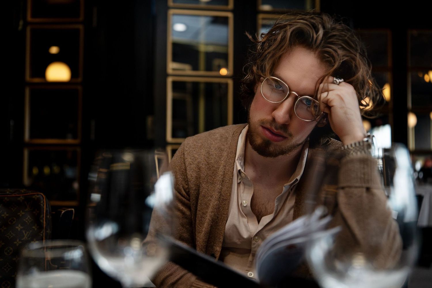 Man in glasses and cardigan looking tired at restaurant table.
