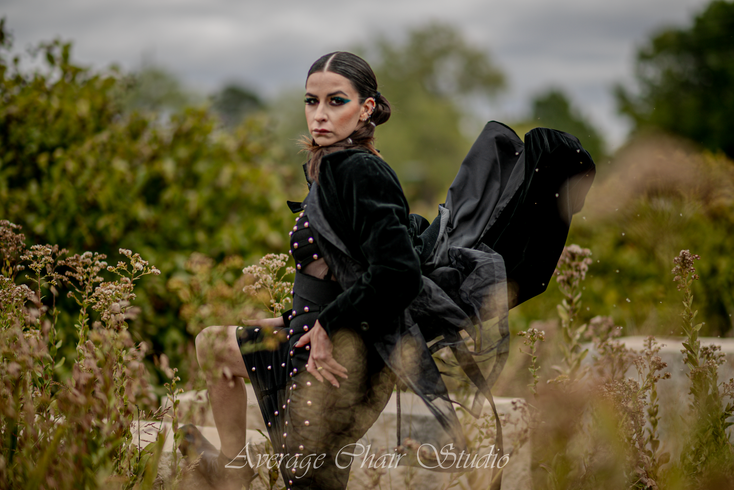 Figure in black dress posing dramatically among wild grasses with flowing fabric.