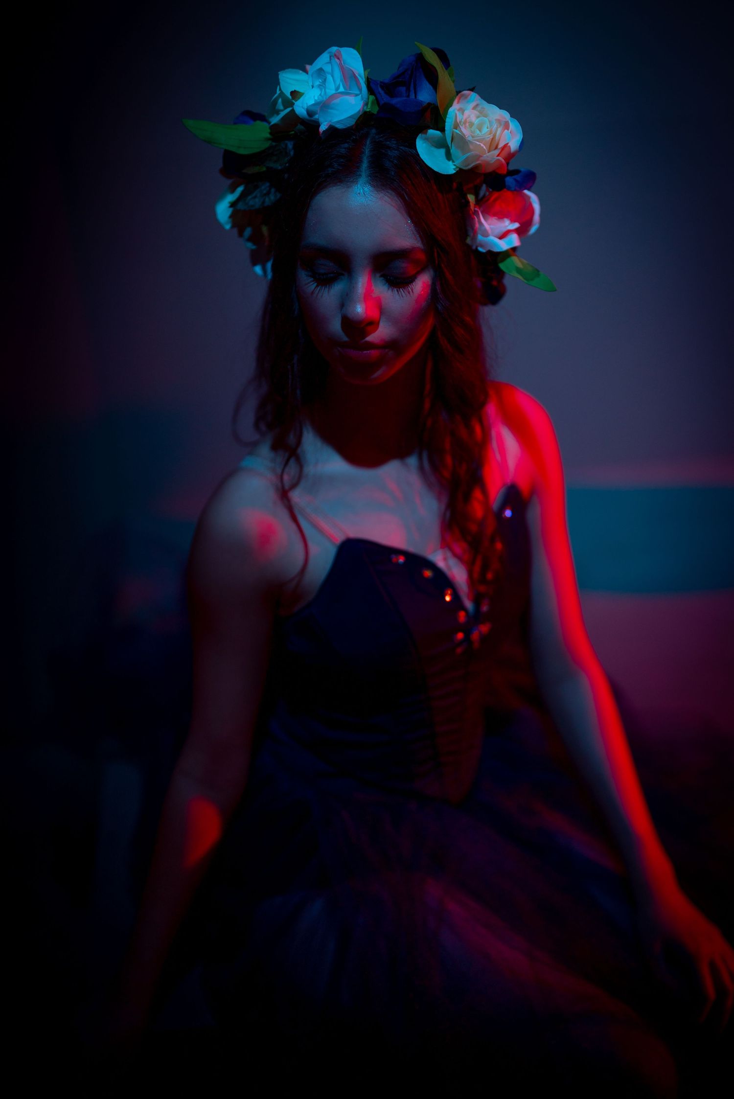Dramatic portrait with floral crown in dark setting illuminated by red and blue lighting effects.
