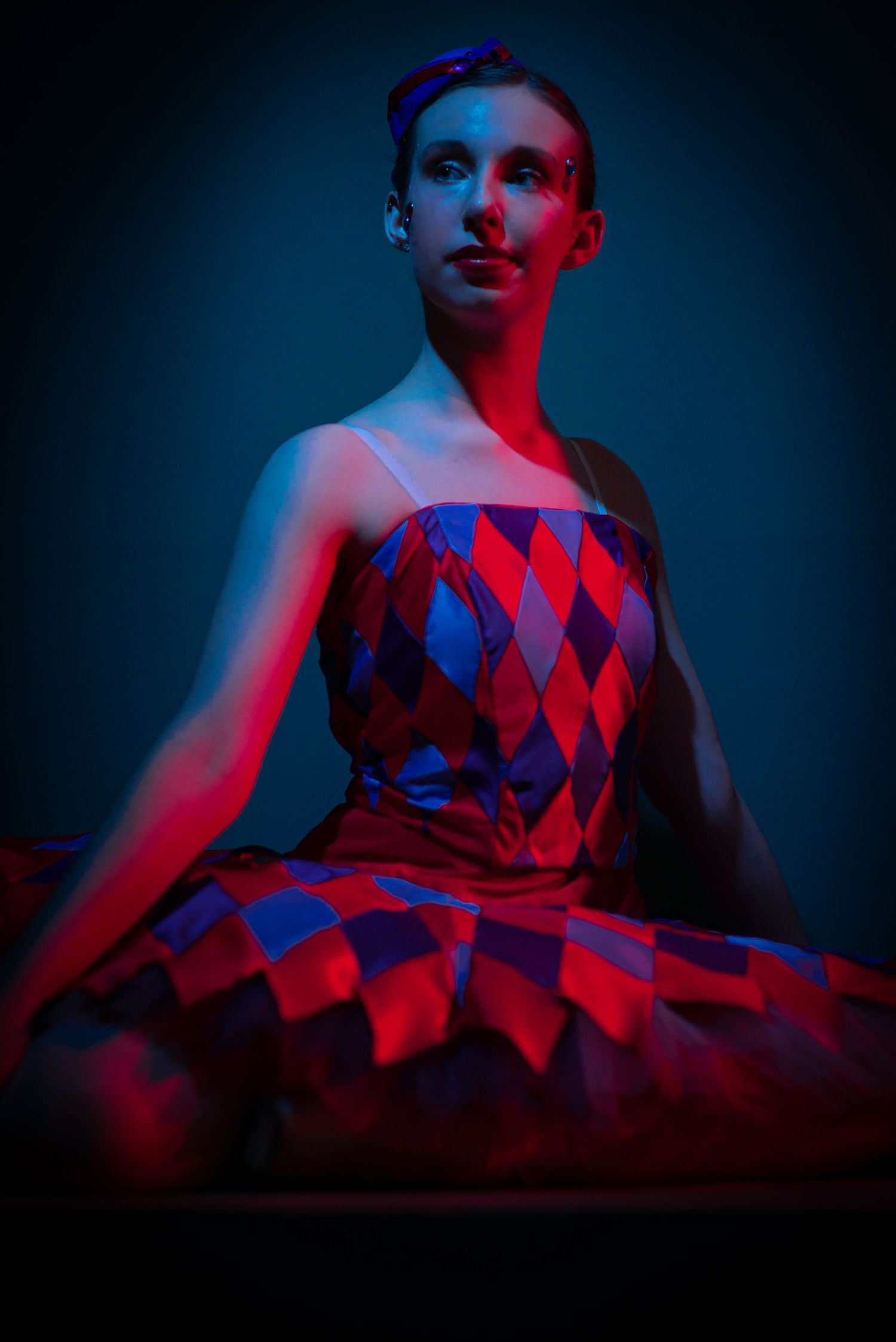Dancer in red and blue diamond pattern dress against dark background.