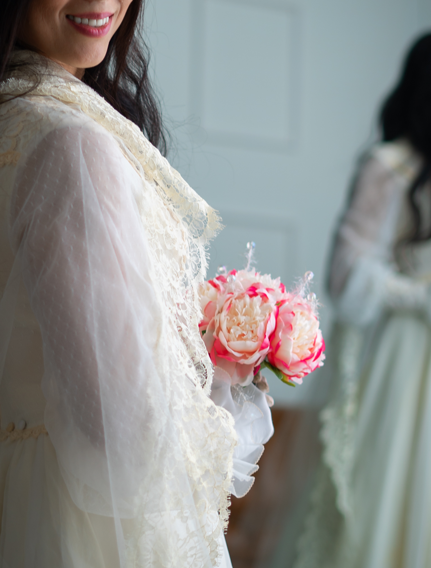 Elegant lace wedding dress detail with pink rose bouquet against white background.