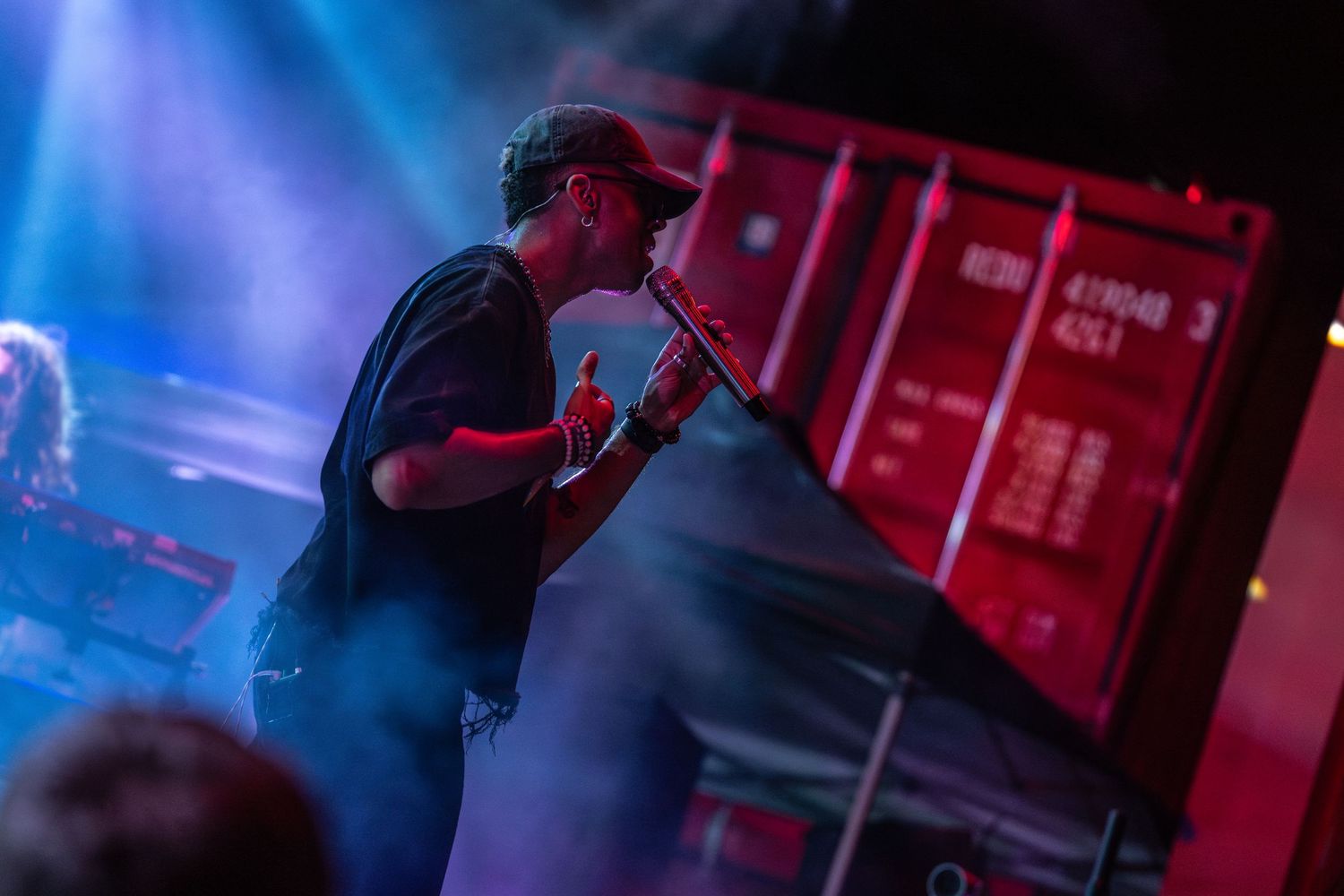A rock musician performs on stage with a guitar while bright pink and blue lights illuminate the performance area.