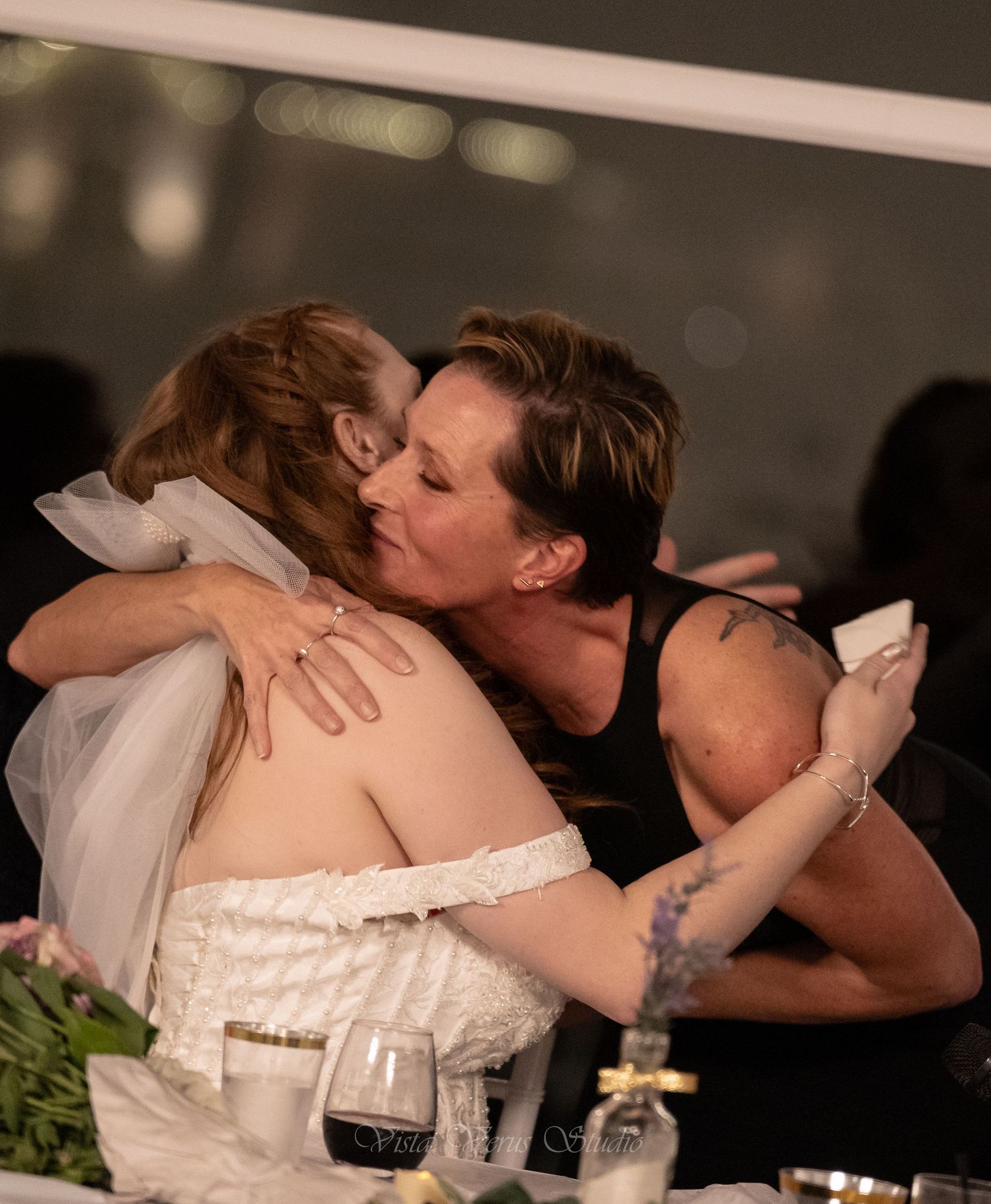 Emotional embrace at wedding reception with table settings and wine glasses.