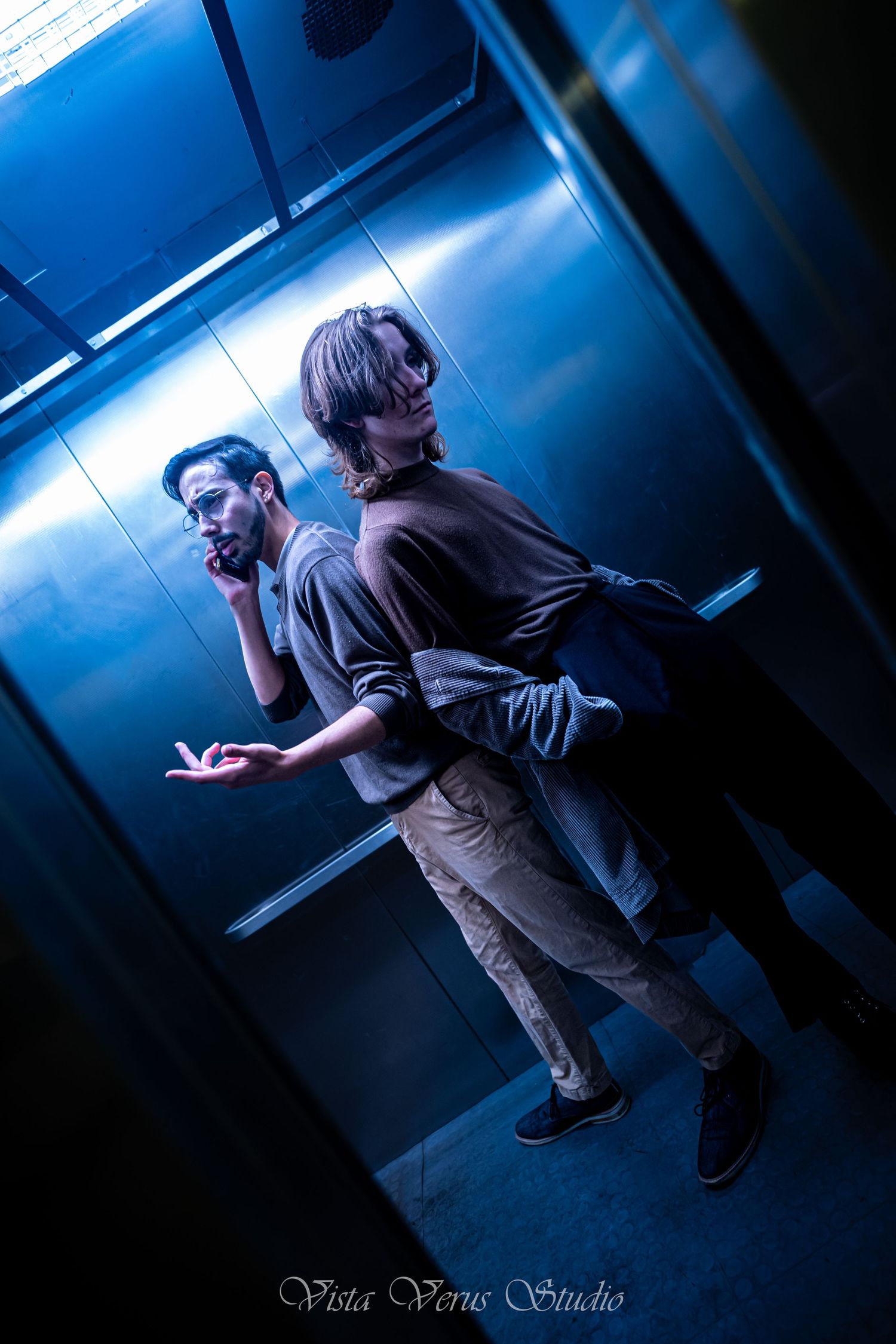 Two people posing dramatically in blue-lit elevator.