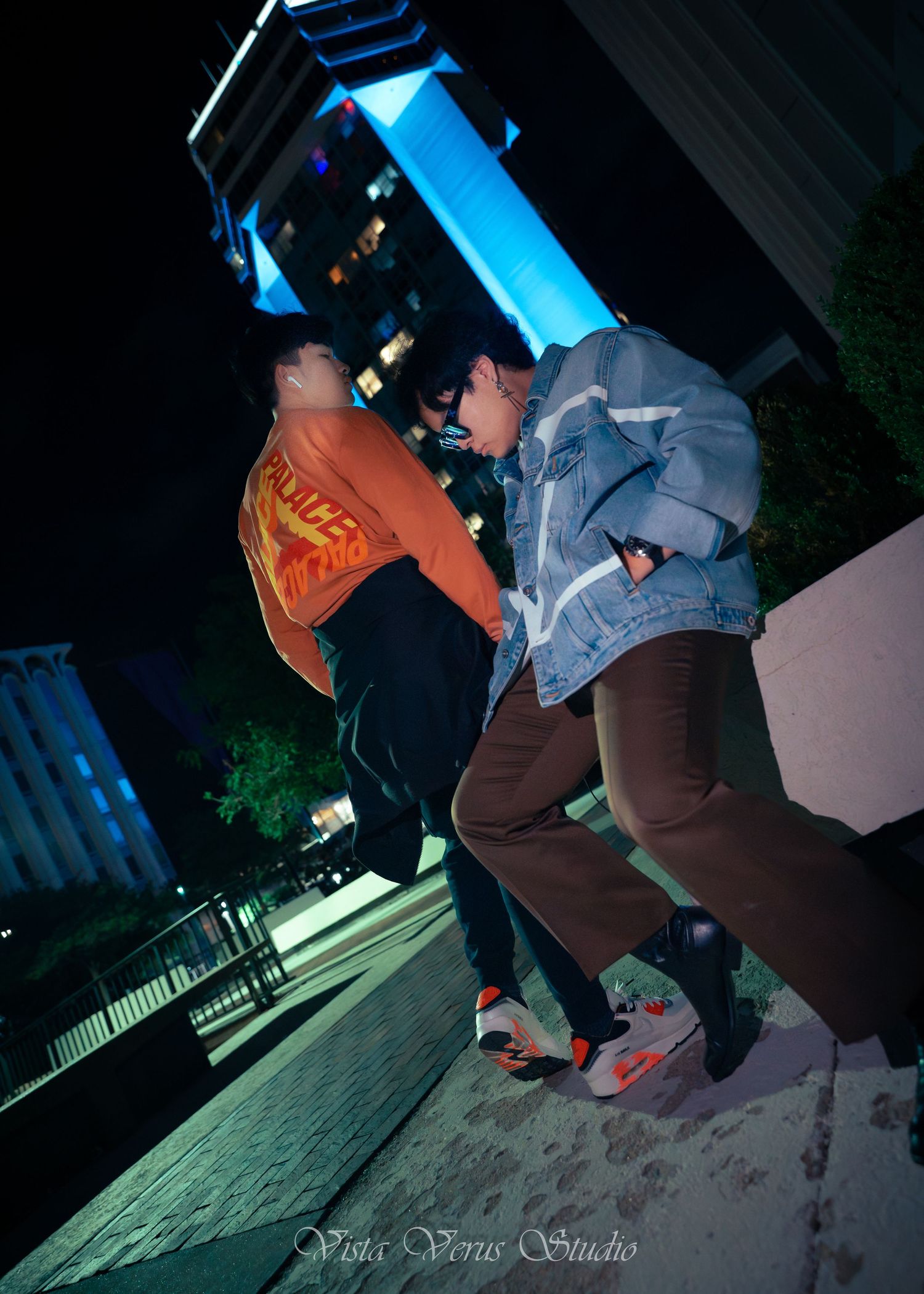 Two people jumping at night on an urban street with dramatic blue lighting.