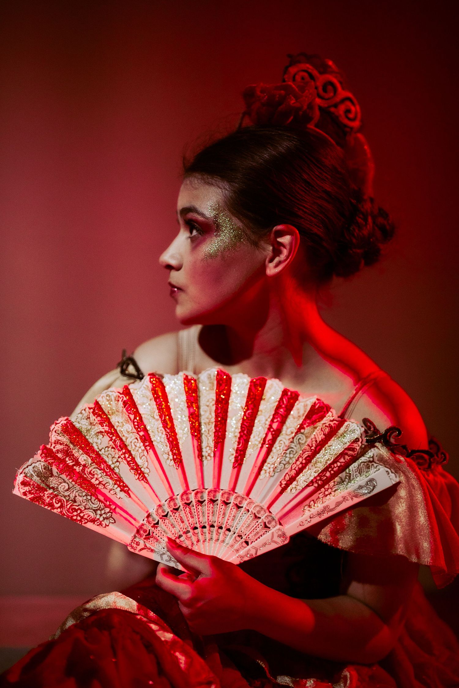 Artistic portrait with lace fan and elegant makeup in red lighting.