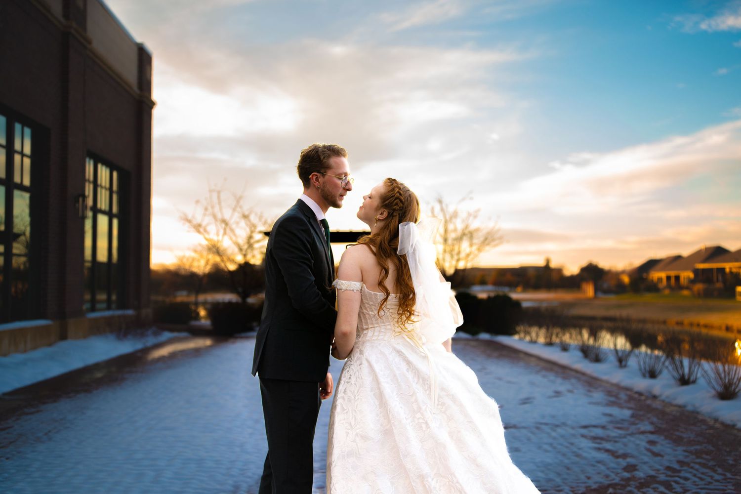 A romantic sunset wedding photo featuring a couple embracing on a pathway beside a reflective pond.