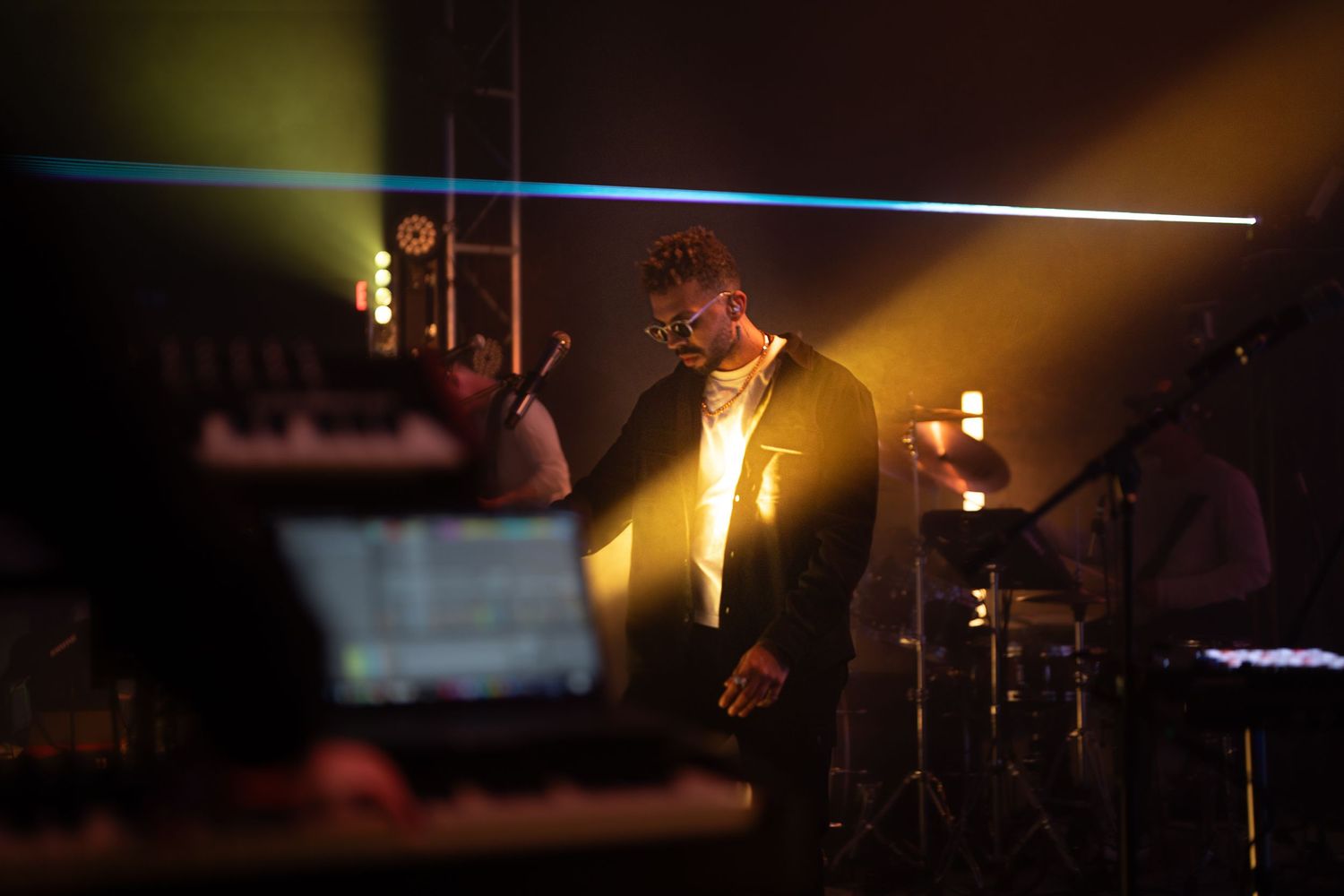 Performer on stage illuminated by dramatic spotlights and beams during a show.