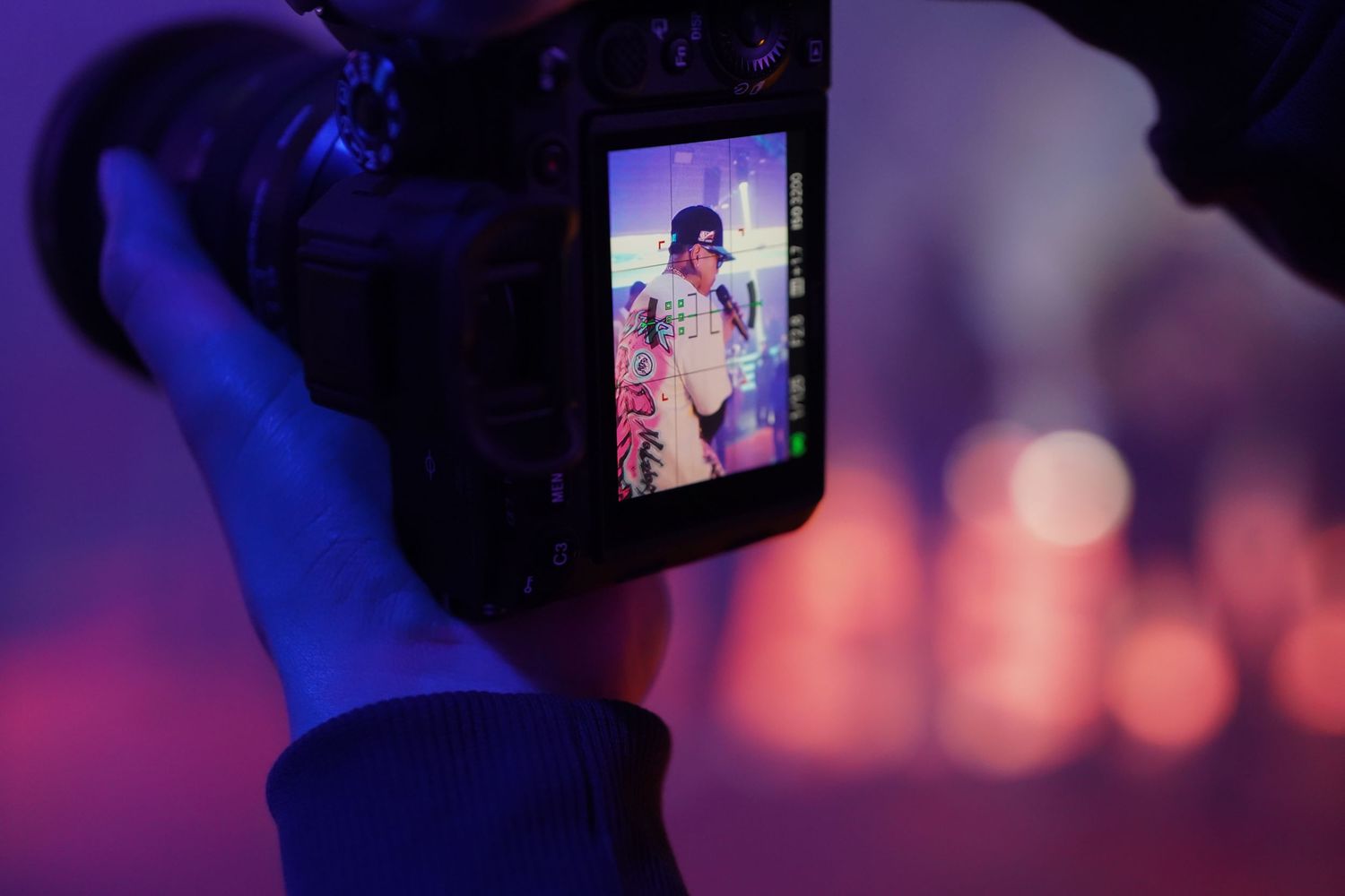 Phone screen displays photo of someone in floral attire against purple and pink bokeh lighting background.