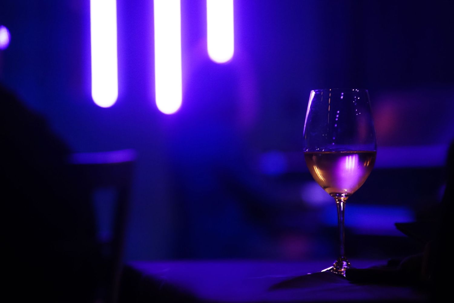 Single wine glass backlit by purple neon tubes creating a dramatic ambiance.
