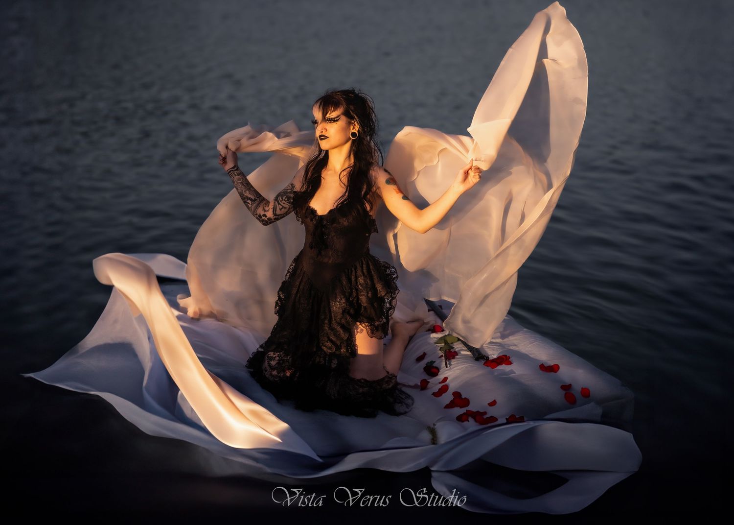 Artistic photo of dancer in black dress with flowing white fabric by water.