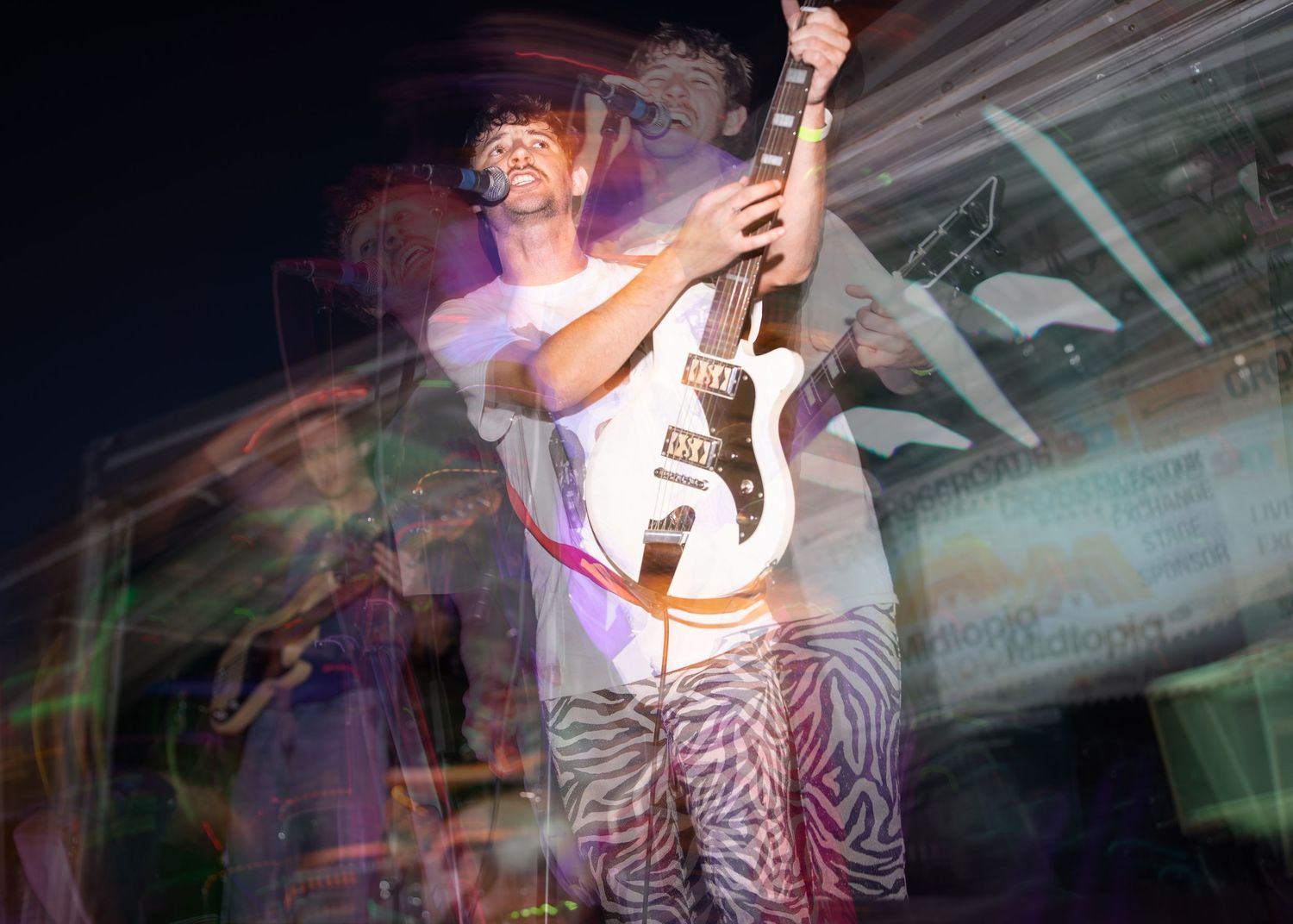 A performer holds a bass guitar on stage with motion blur effects and colorful lighting creating a dynamic atmosphere.