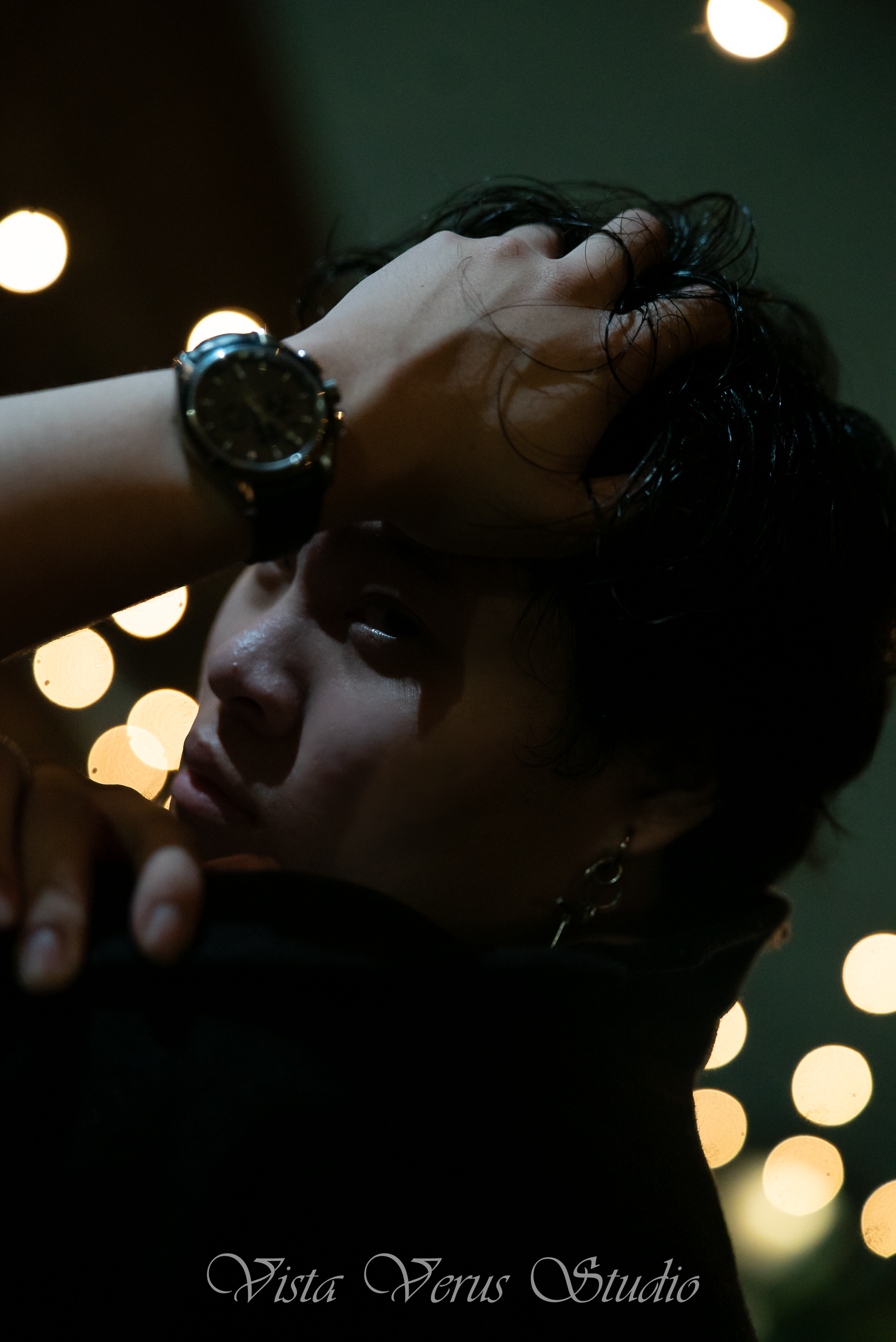Artistic portrait in low light with bokeh highlights and a wristwatch detail.