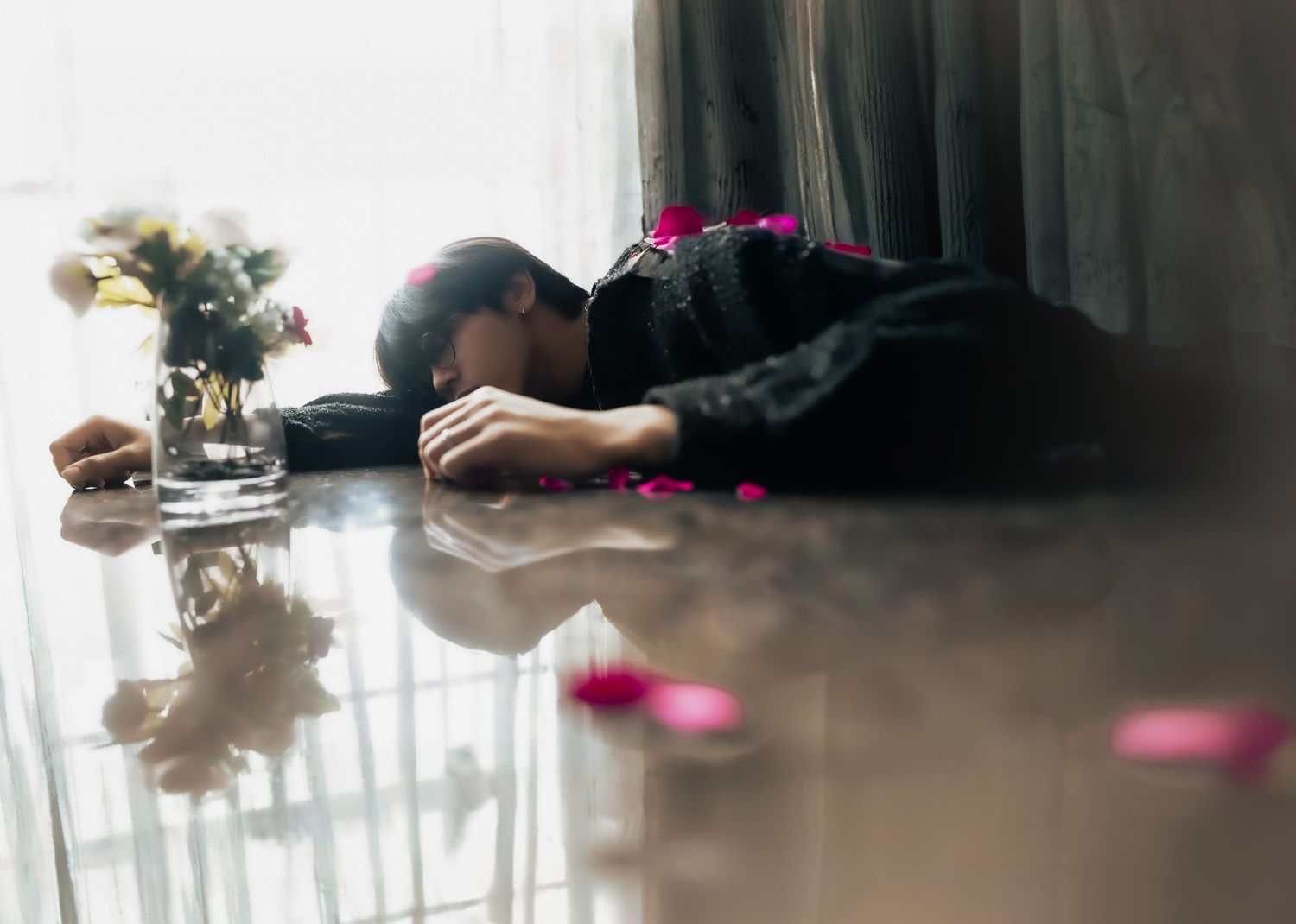 Moody scene with scattered pink petals on reflective surface.