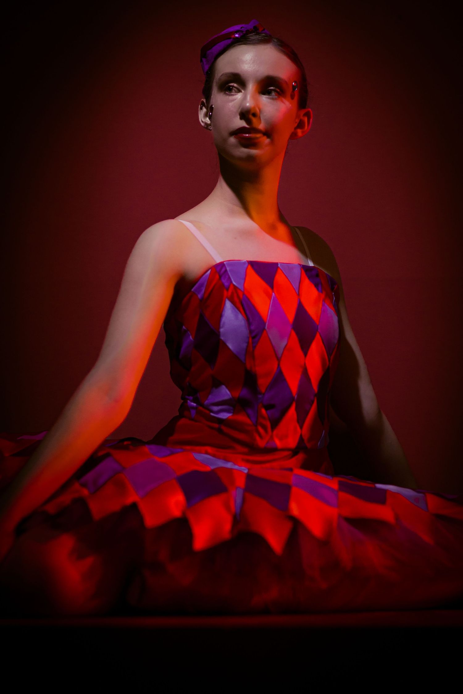 A ballet dancer in a dramatic red and purple geometric patterned dress poses under moody lighting.