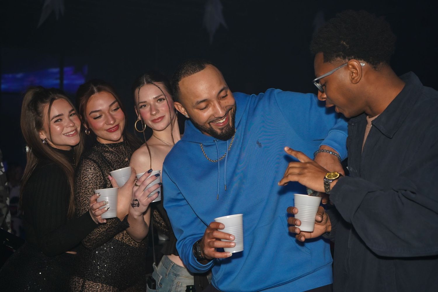 Group of friends laughing and having drinks together at a dimly lit nightclub or party.