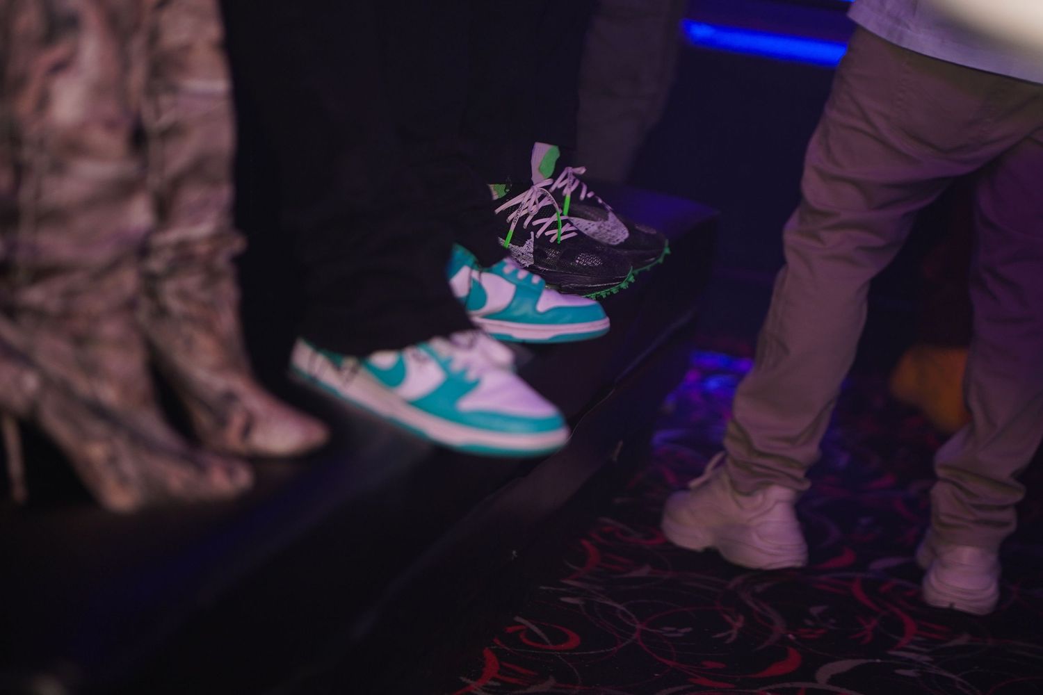 Colorful sneakers illuminated by blue lighting on a dark dance floor during a nighttime event or party.