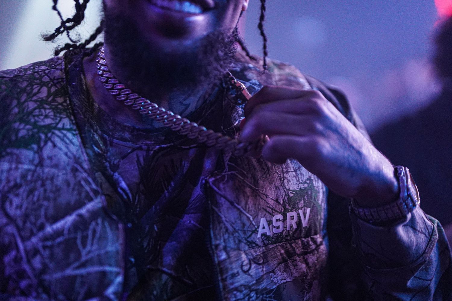 Close-up shot of person wearing ASRV jacket in dark purple lighting.