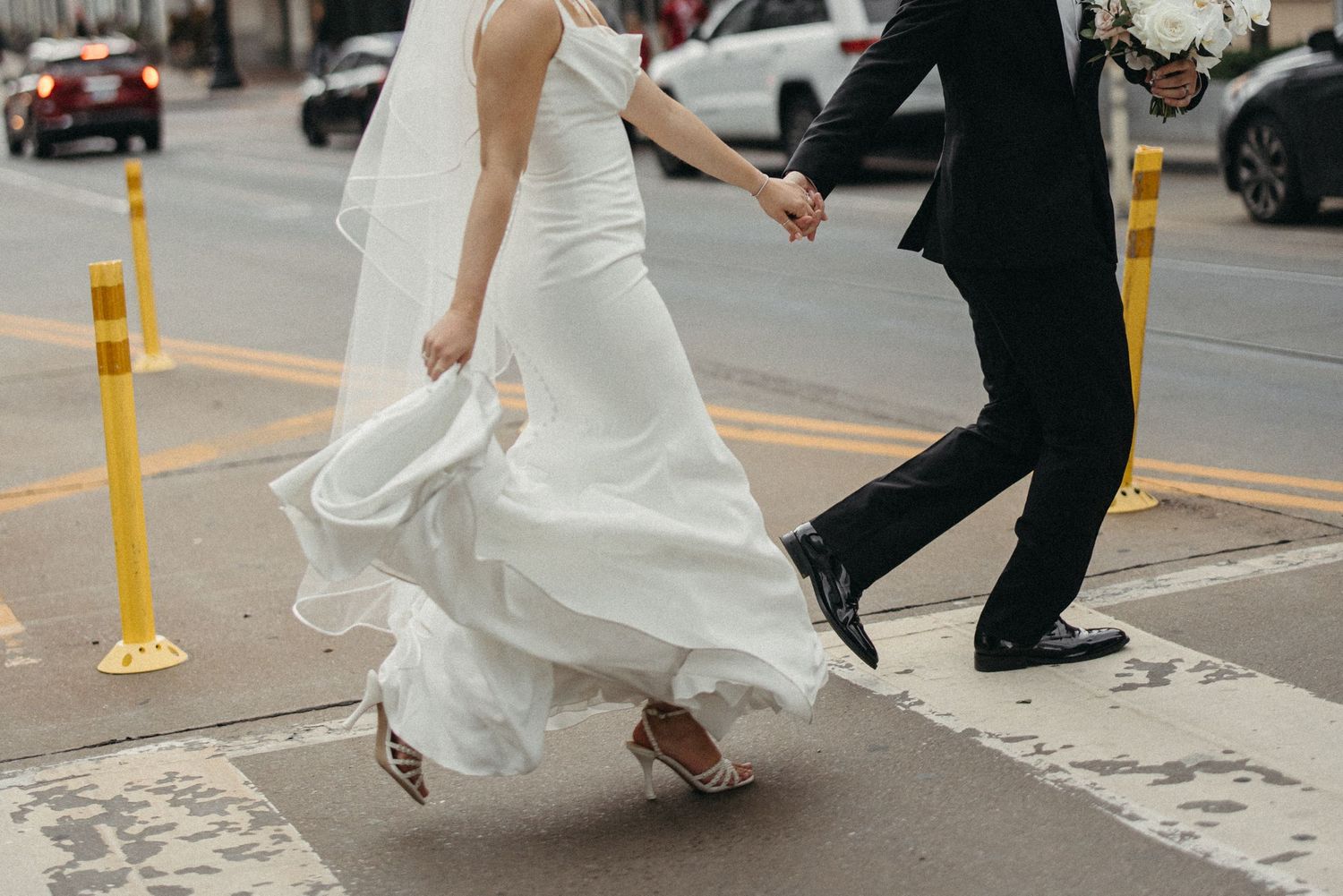 Bride in white wedding dress walking down city street with dress flowing behind her.