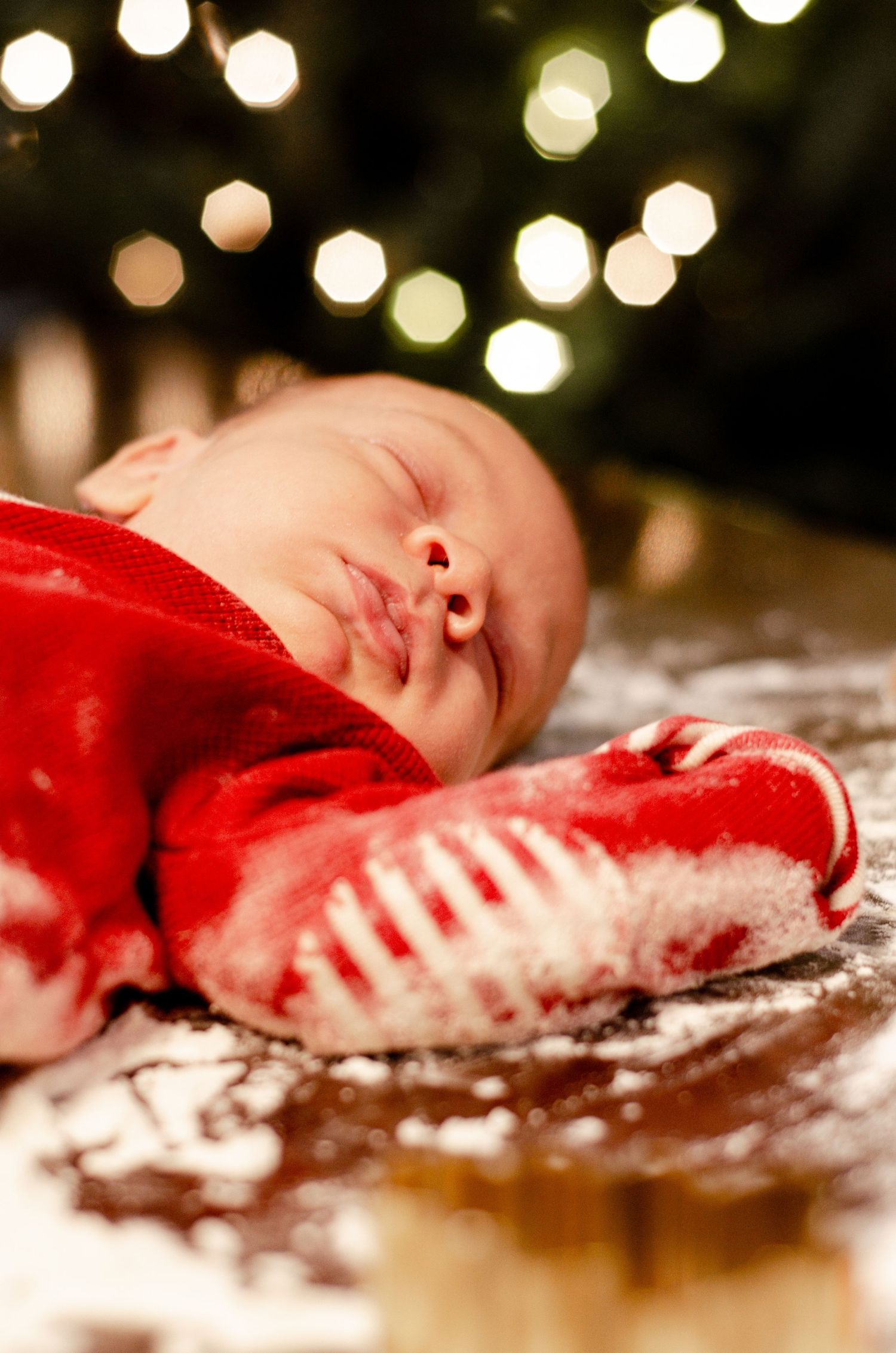 Peaceful sleeping baby in red outfit with twinkling holiday lights in background. Newborn photography in Columbus, OH