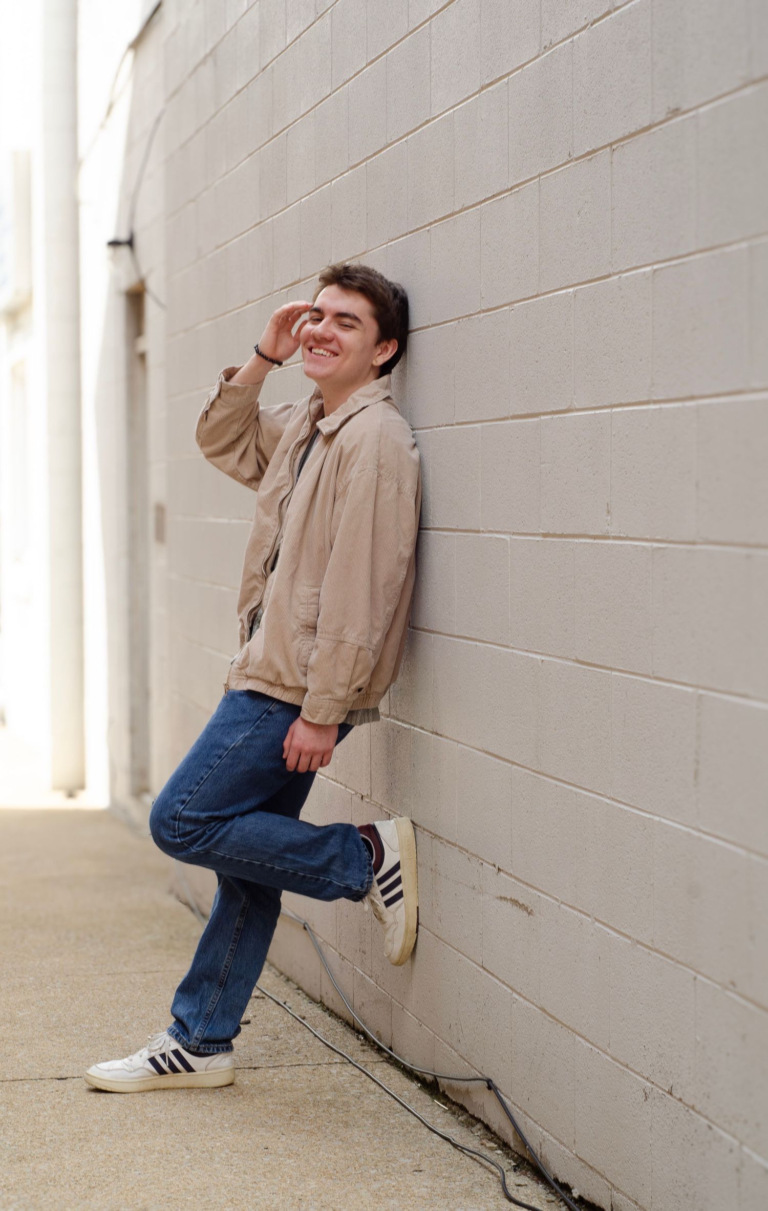A candid laughing pose against a white wall wearing casual attire.