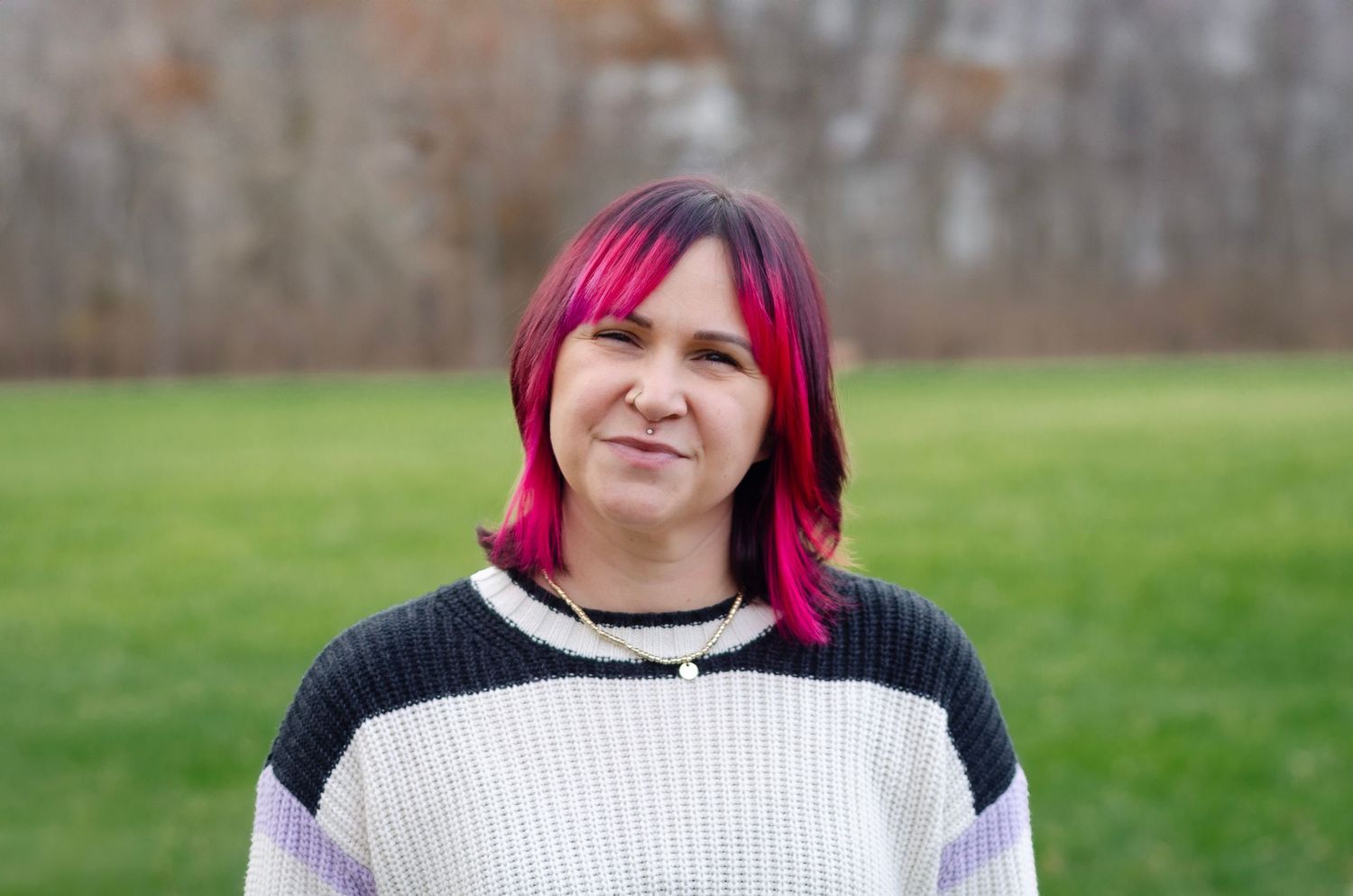 Portrait featuring bright pink hair and black and white sweater outdoors.