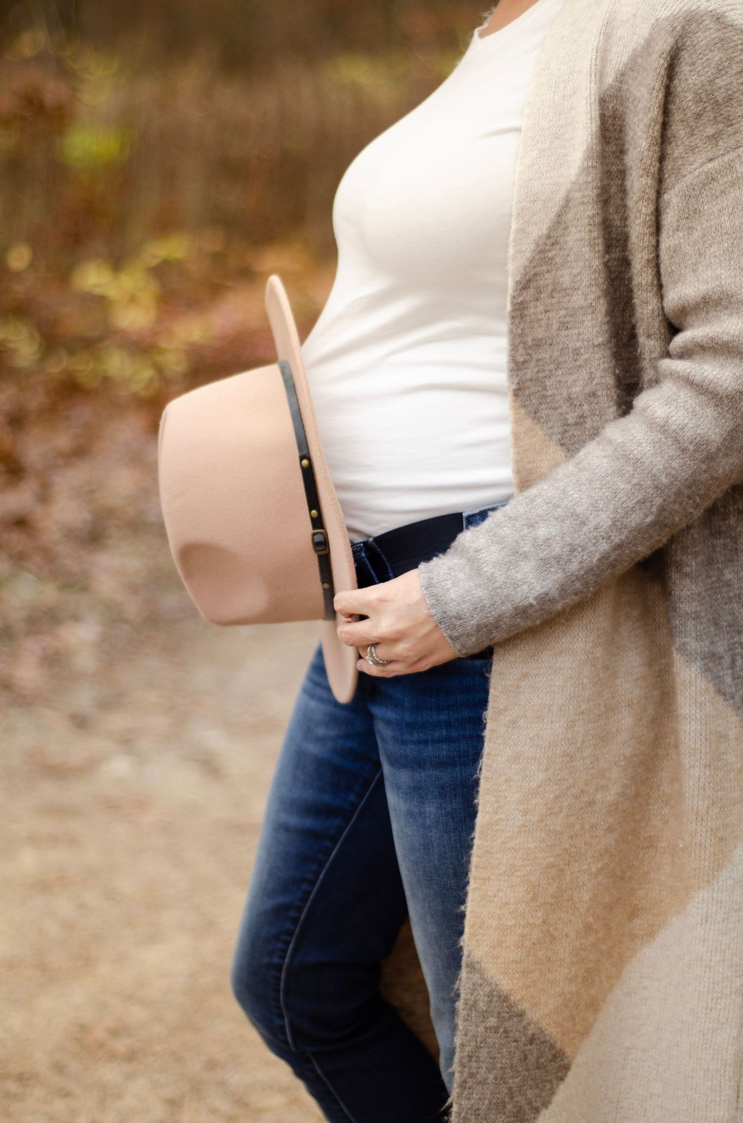 Side view of a pregnant woman wearing jeans and gray cardigan.