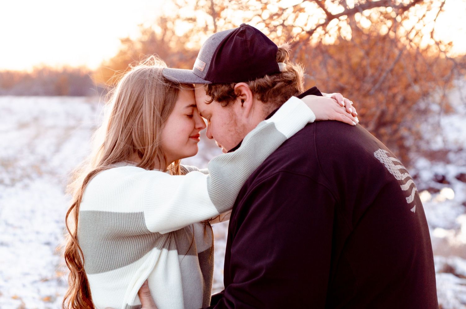 Couple embracing in a tender moment during winter with snow-covered scenery behind them.