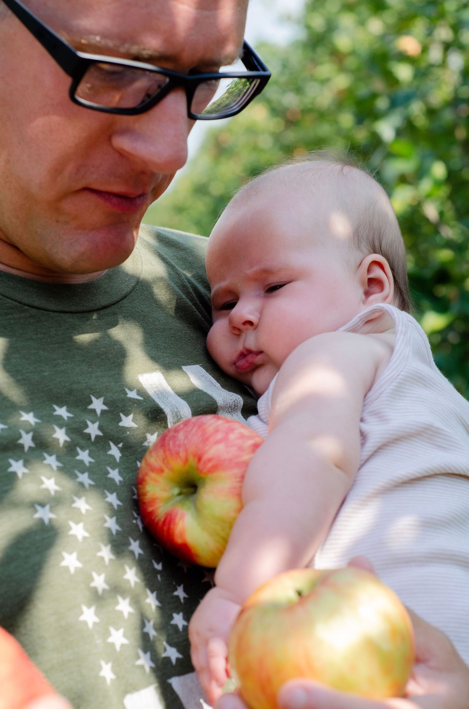 Sweet candid moments captured outdoors with sunlit apple and gentle embraces. Family photos by KM Conceptions Photography in Columbus, OH.
