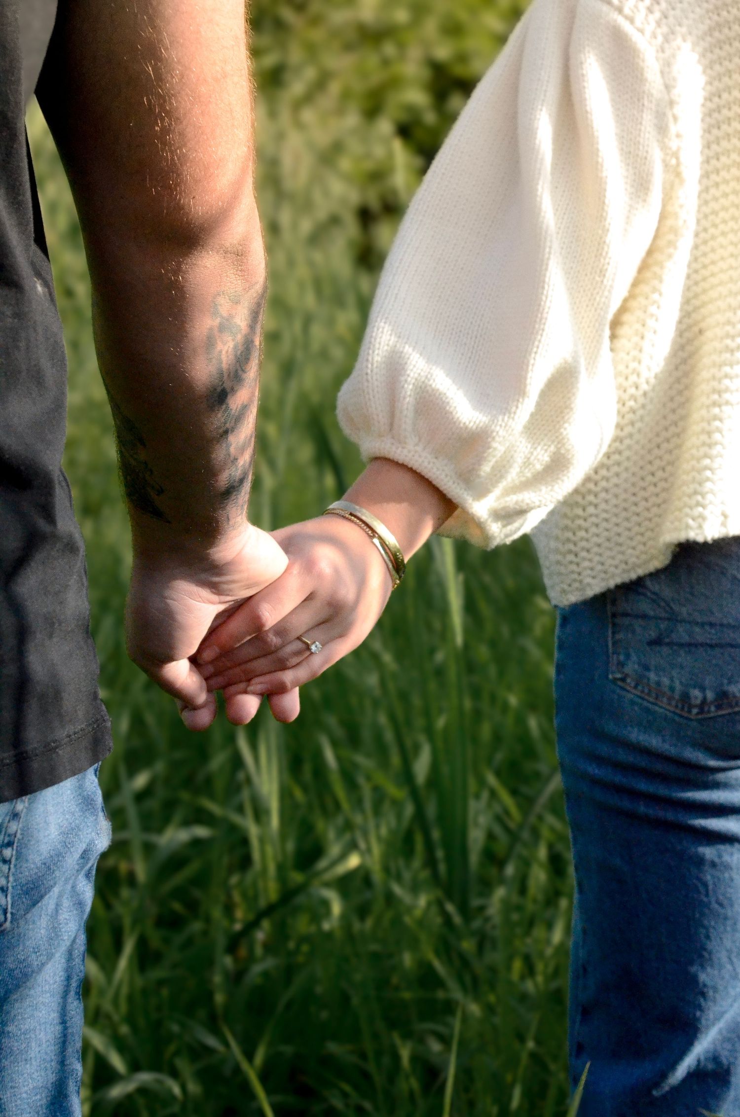 Person wearing cream sweater and jeans standing in tall grass during golden hour. Engagement photos by KM Conceptions Photography