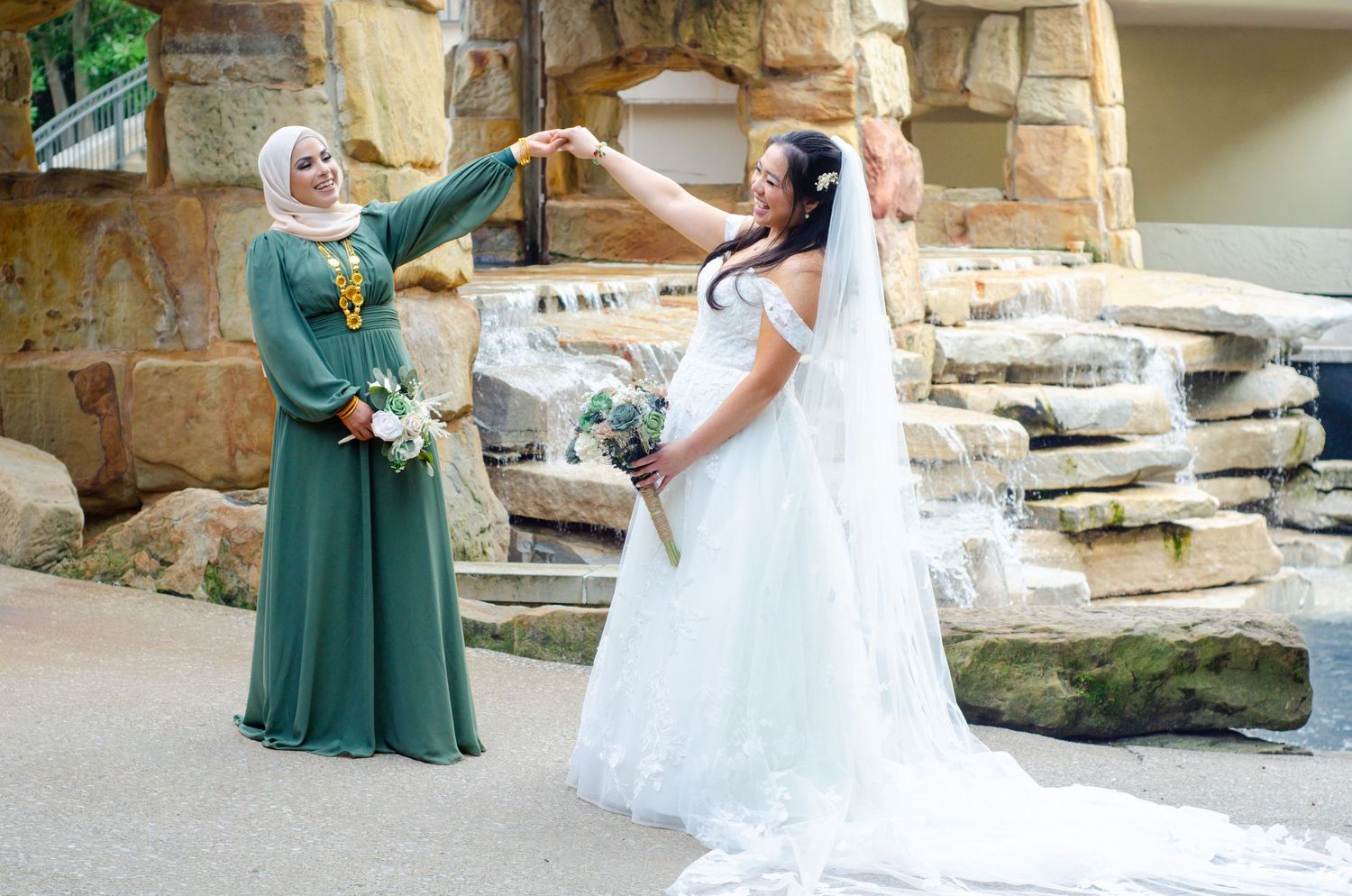 Wedding party members in green dresses and white gown pose playfully in outdoor garden setting.