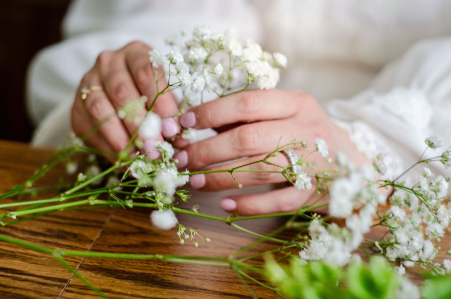 Close-up shots of hands arranging delicate white baby's breath flowers on a wooden surface. Wedding photos by KM Conceptions Photography