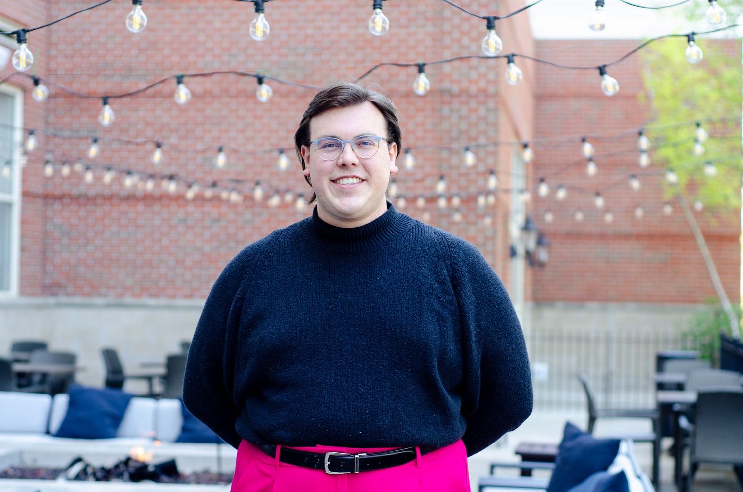 Professional portrait against brick wall with string lights showing person in black sweater.