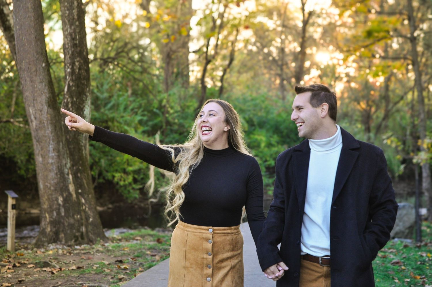 Joyful couple laughs together while walking through autumn woods at sunset.