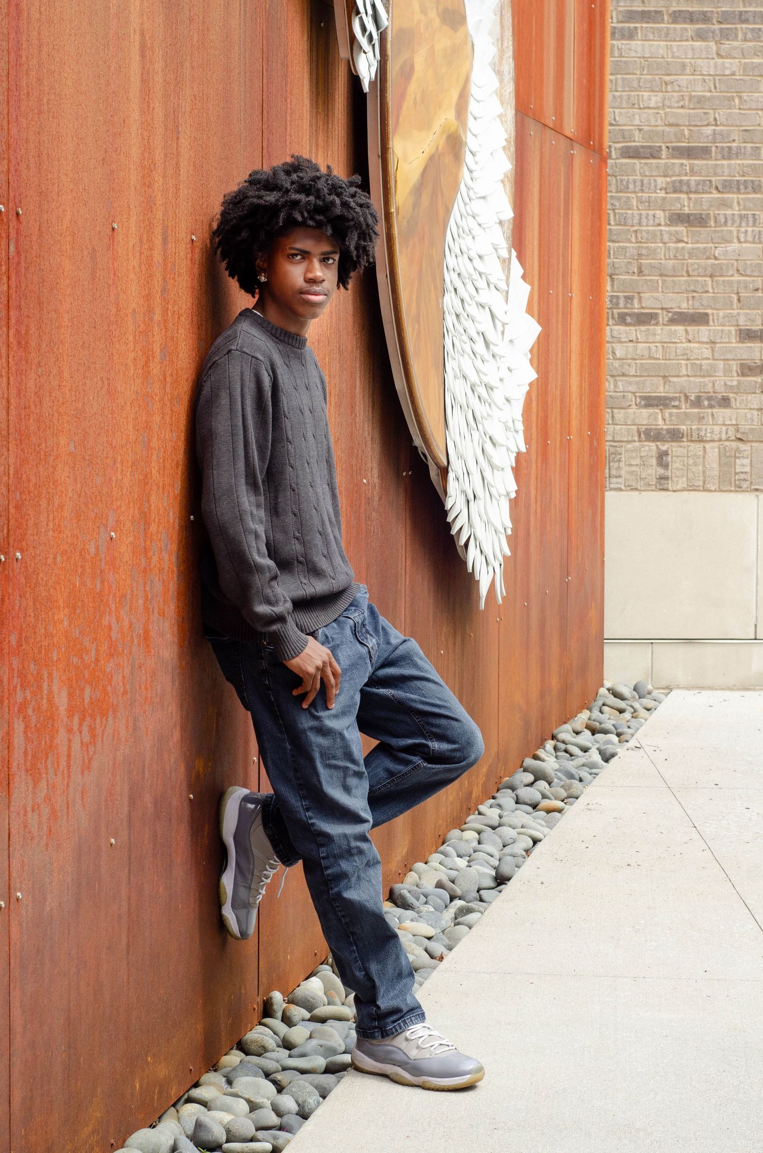 Person in casual attire leans against orange wall with decorative wing installation.